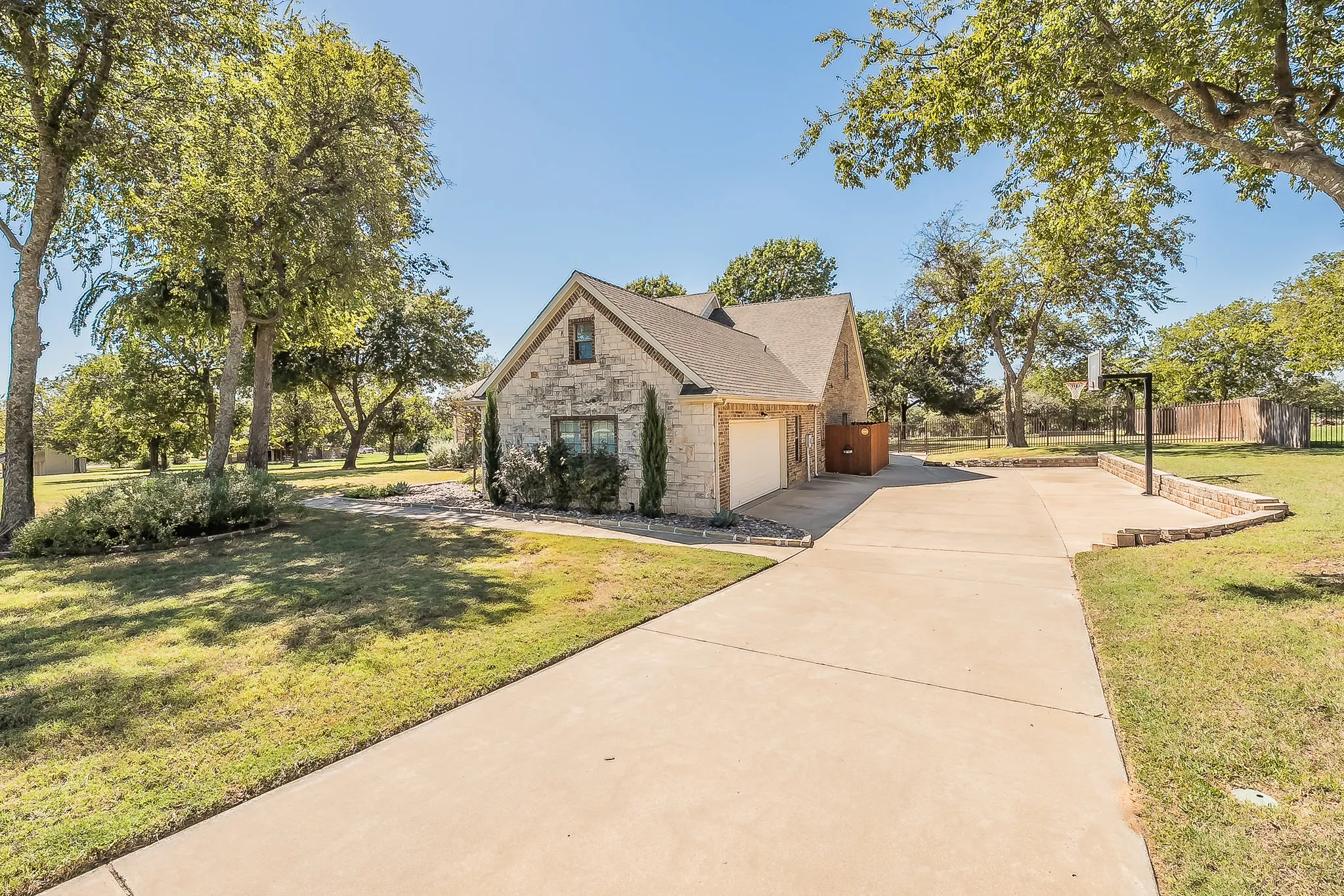 Stone facade residence featuring a front-facing attached garage, concrete driveway, and established landscaping