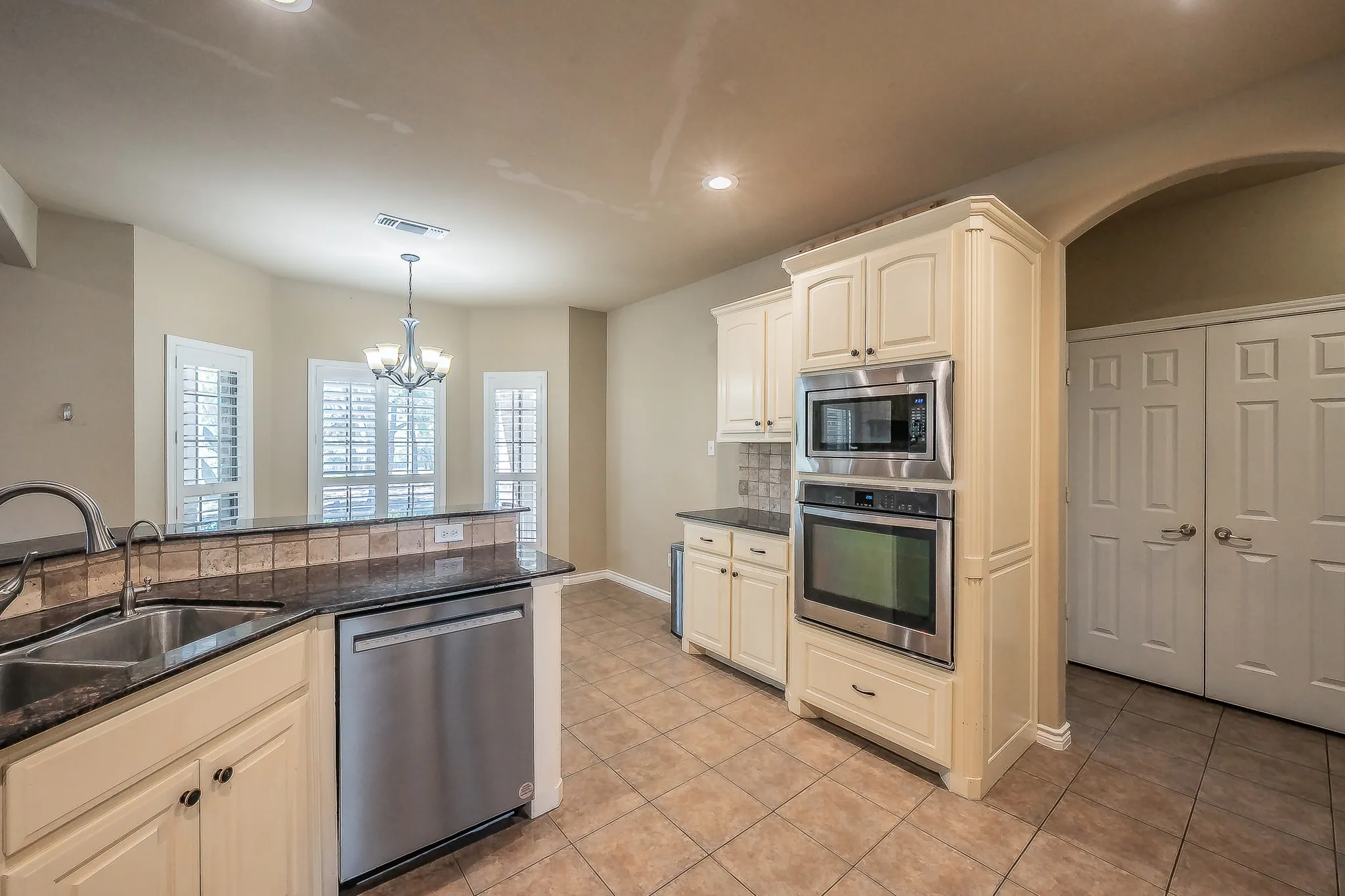 Cream cabinetry with dark stone countertops, stainless steel appliances, a double basin sink, and tile flooring