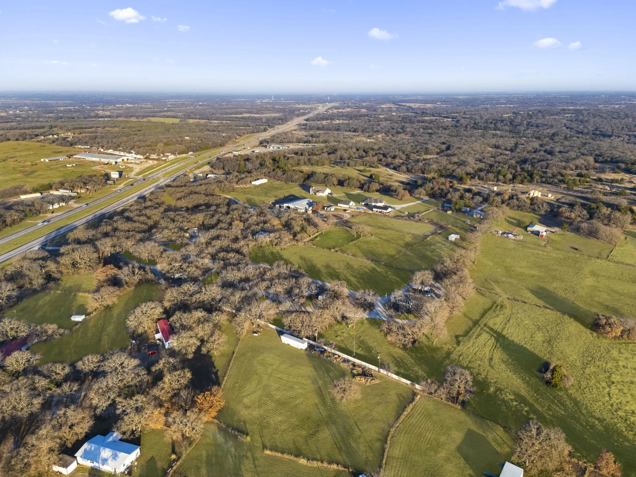 Expansive land parcel featuring open green fields, extensive tree coverage, and a paved highway in the distance