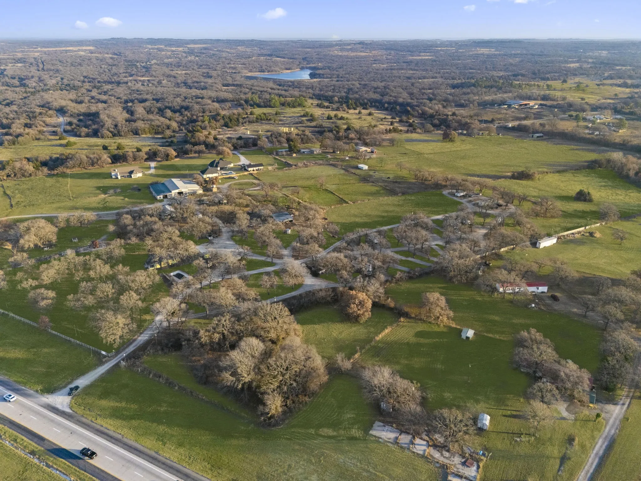 Expansive property featuring lush green fields, scattered mature trees, multiple outbuildings, and a large main structure