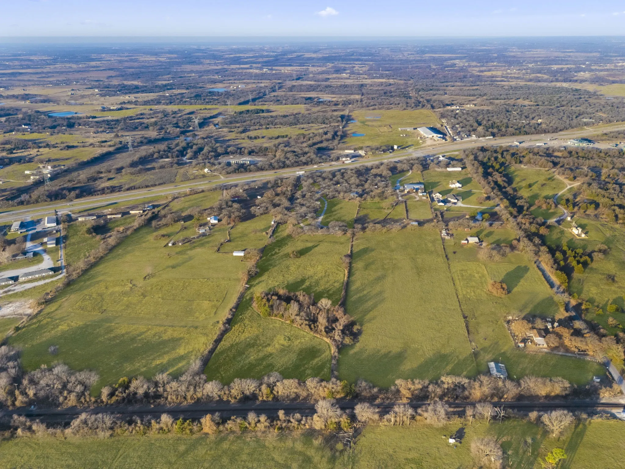 Expansive rural landscape featuring green fields, scattered trees, and distant structures