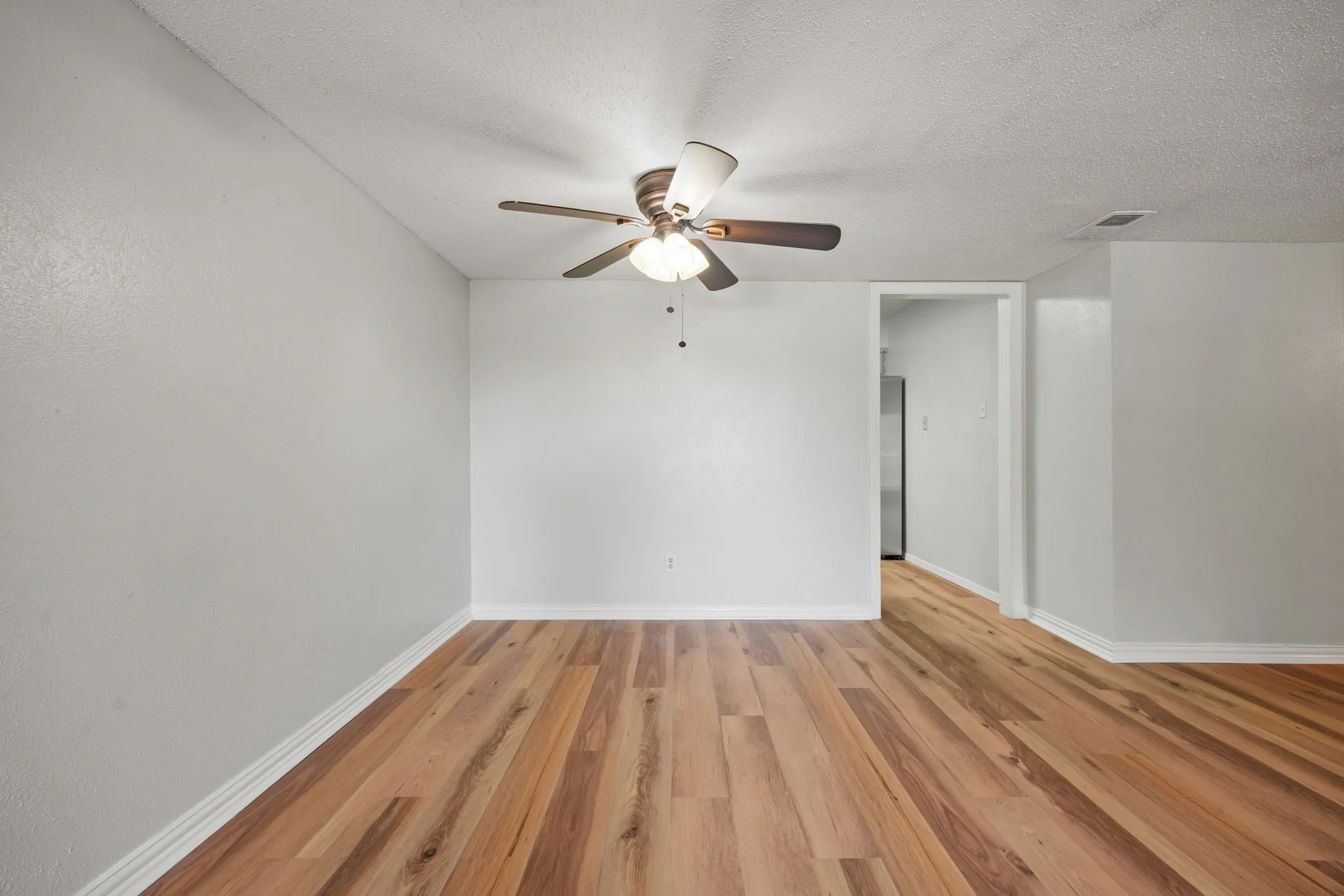 Spacious room featuring wood-finish flooring, light gray walls, and a ceiling fan with integrated lighting