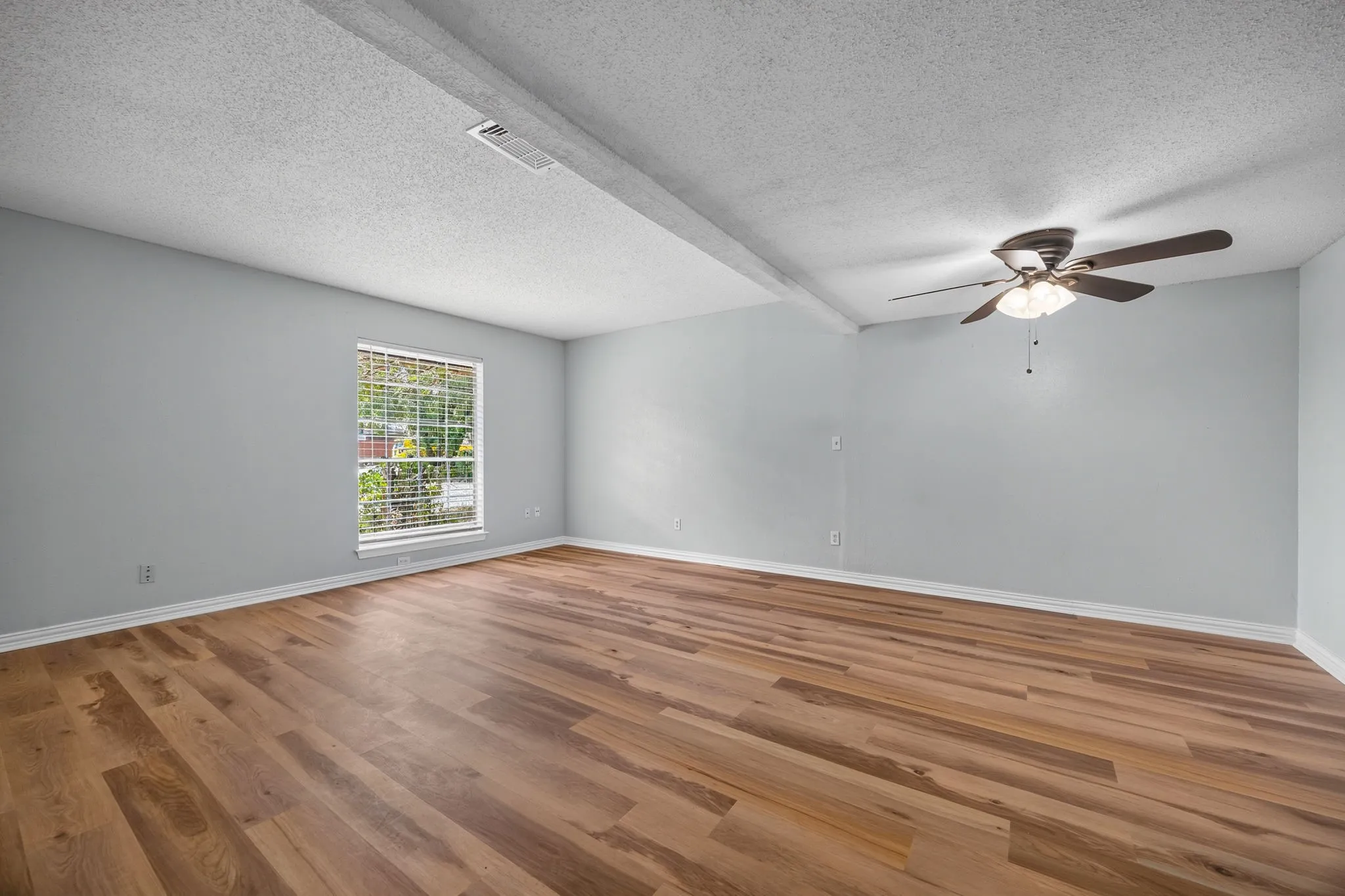 Spacious room featuring wood-finish flooring, light gray walls, white trim, and a ceiling fan with integrated lighting