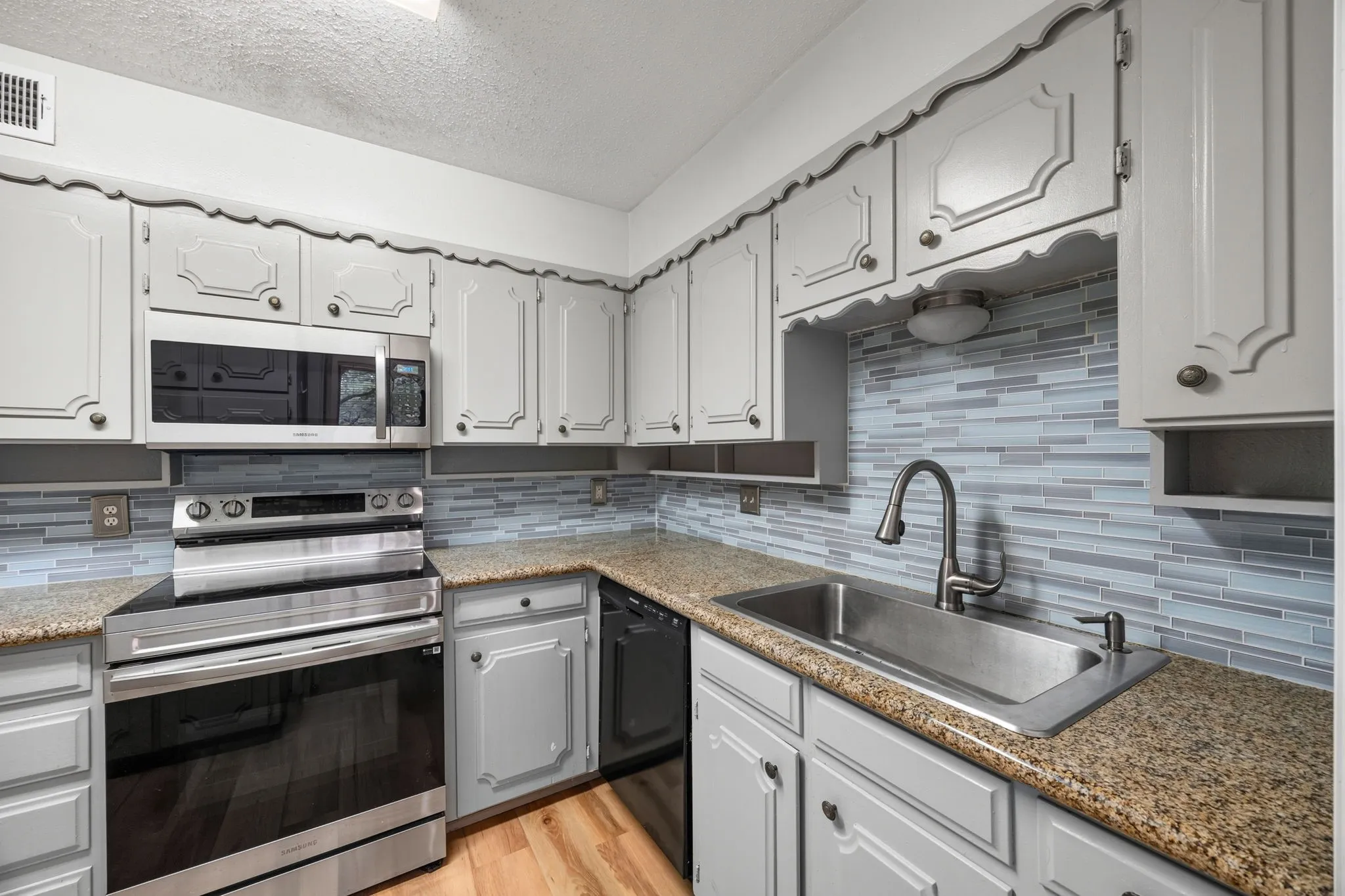 Kitchen featuring light gray cabinetry, stainless steel appliances, a mosaic tile backsplash, a stainless steel sink with a gooseneck faucet, and wood-finish flooring