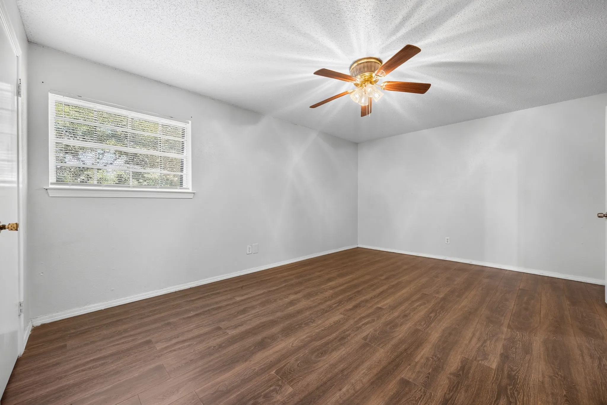 Spacious interior featuring wood-finish flooring, light gray walls, a ceiling fan with integrated lighting, a window with horizontal blinds, and white trim throughout