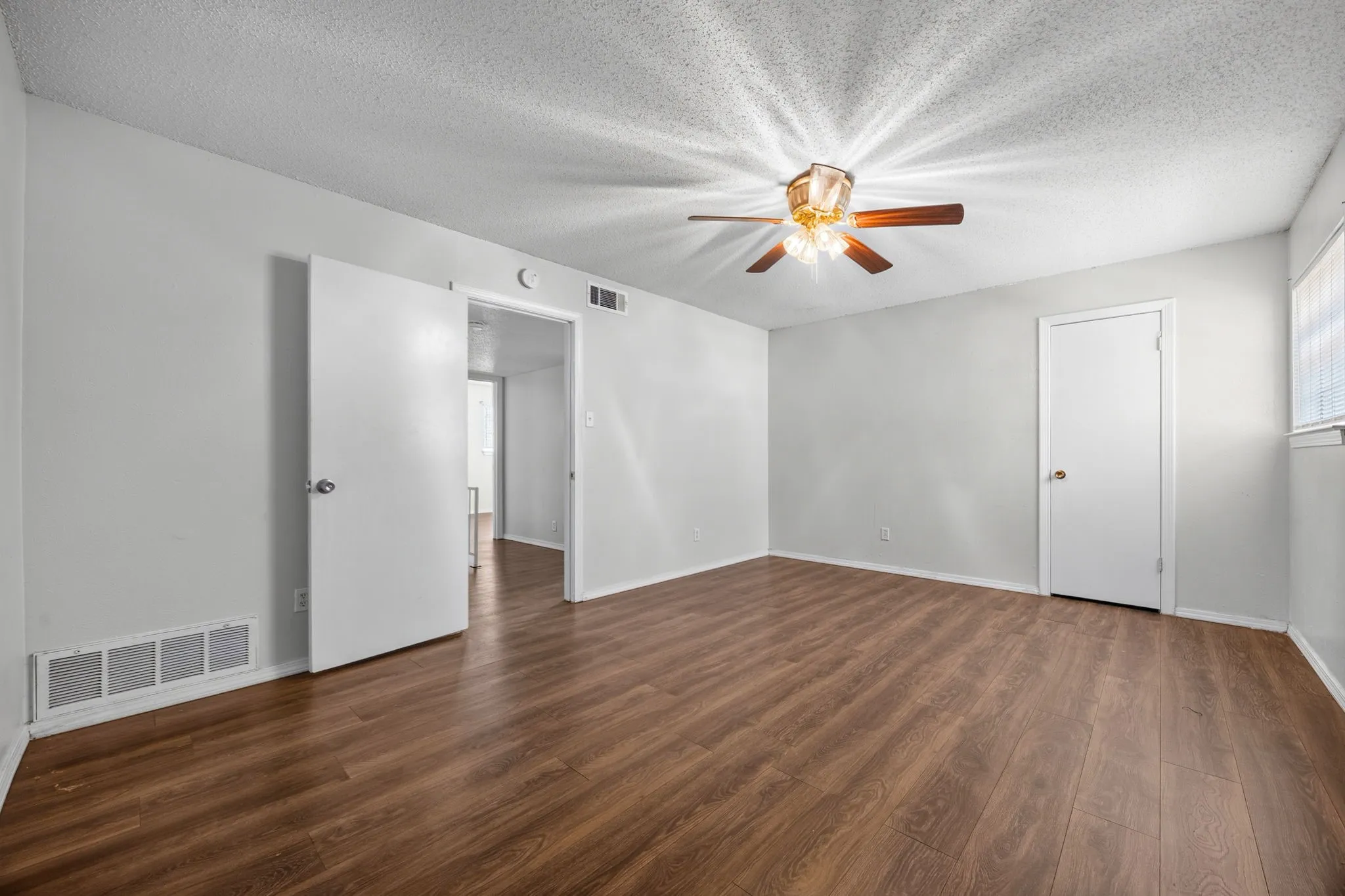 Room featuring wood-finish flooring, white walls, and a ceiling fan with integrated lighting