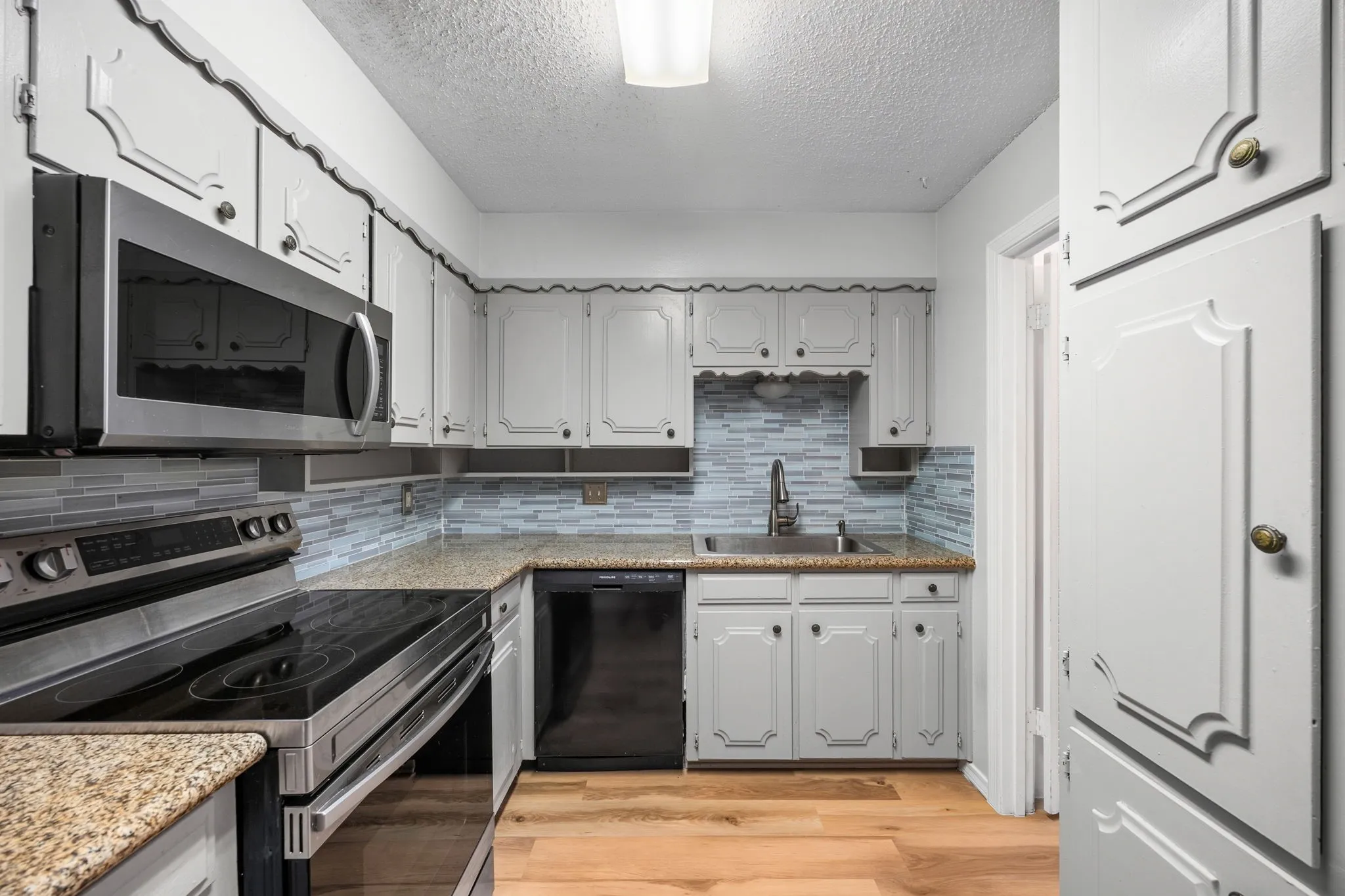 Kitchen featuring granite countertops, light-finish cabinetry, stainless steel microwave, black electric range, and wood-finish flooring