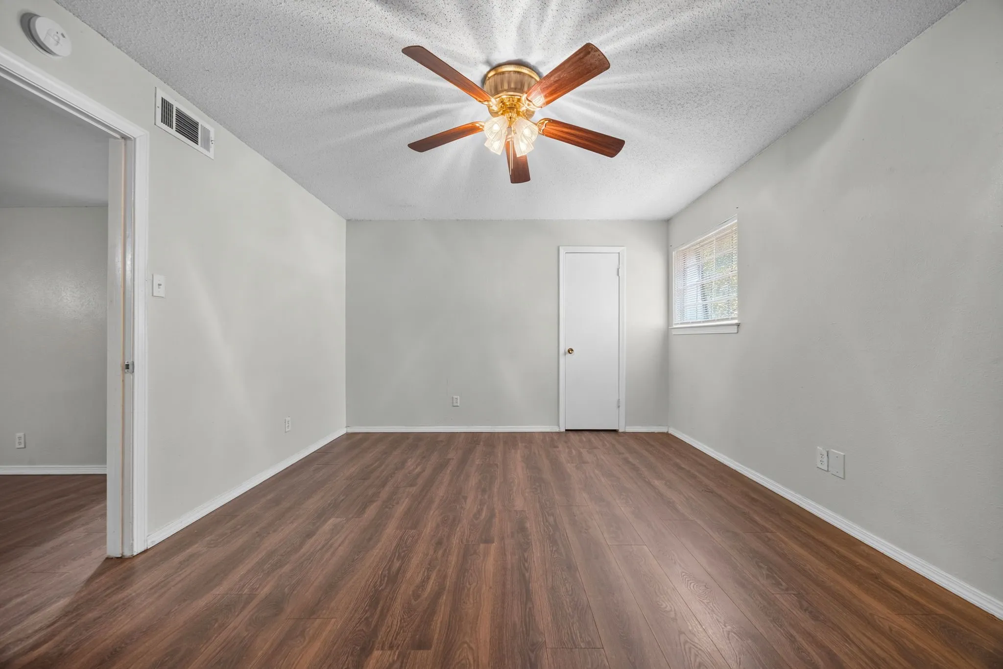 Spacious room featuring wood-finish flooring, light gray wall paint, and a ceiling fan with integrated lighting