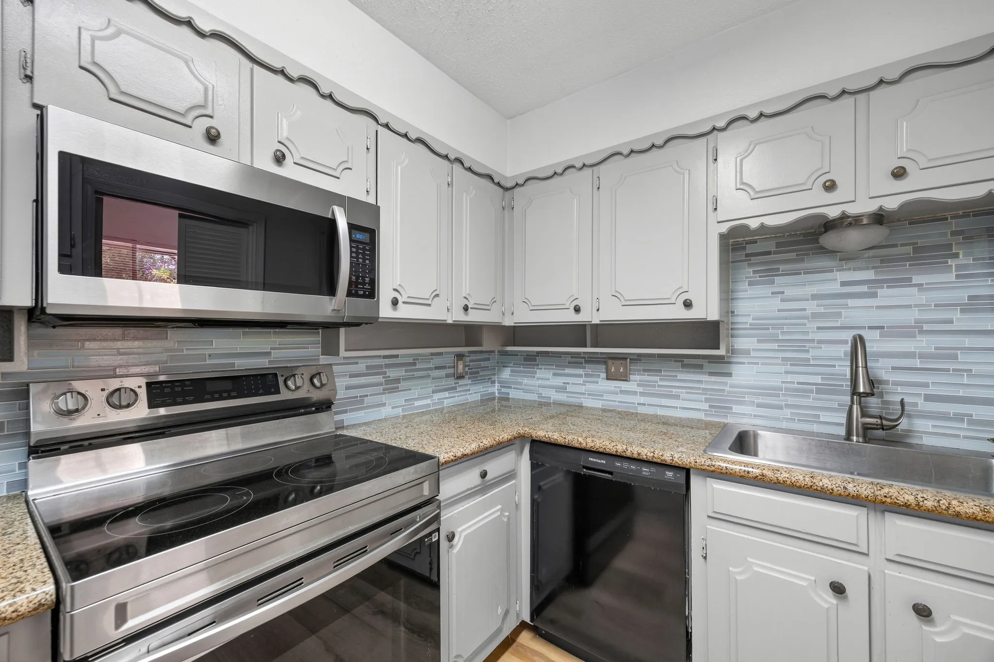 Kitchen featuring light-toned cabinetry with decorative trim, granite countertops, and a full tile backsplash