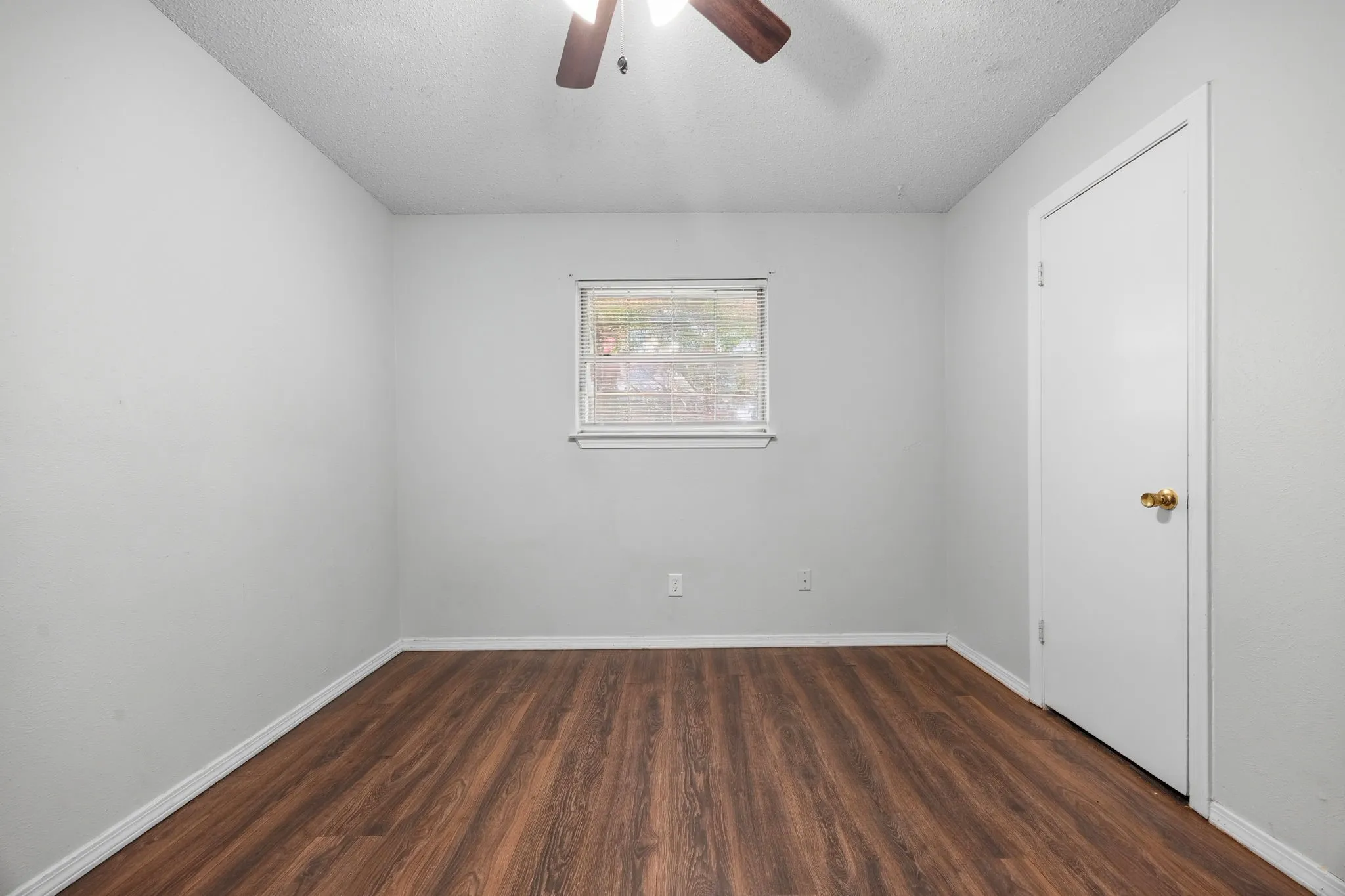 Room featuring wood-finish flooring, light gray walls, a single window with blinds, and a white interior door