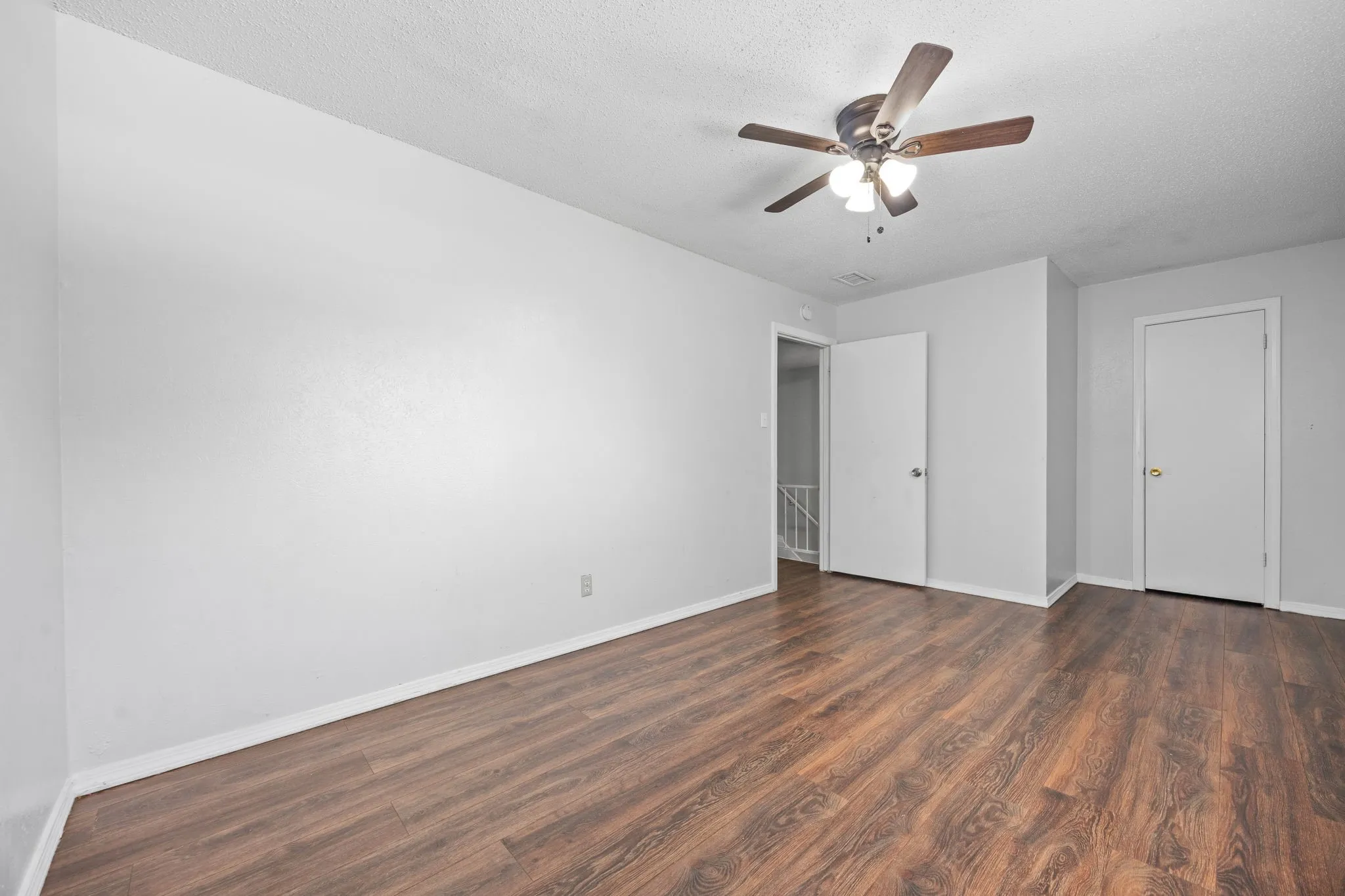 Spacious room featuring wood-finish flooring, light gray walls, and a ceiling fan with integrated lighting