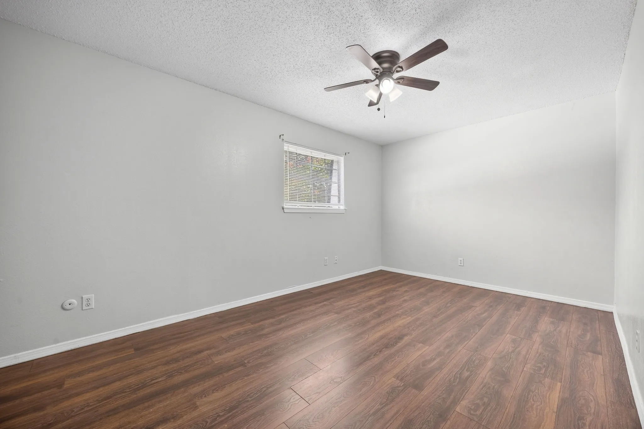 Spacious interior featuring wood-finish flooring, a ceiling fan with integrated lighting, and a window with blinds
