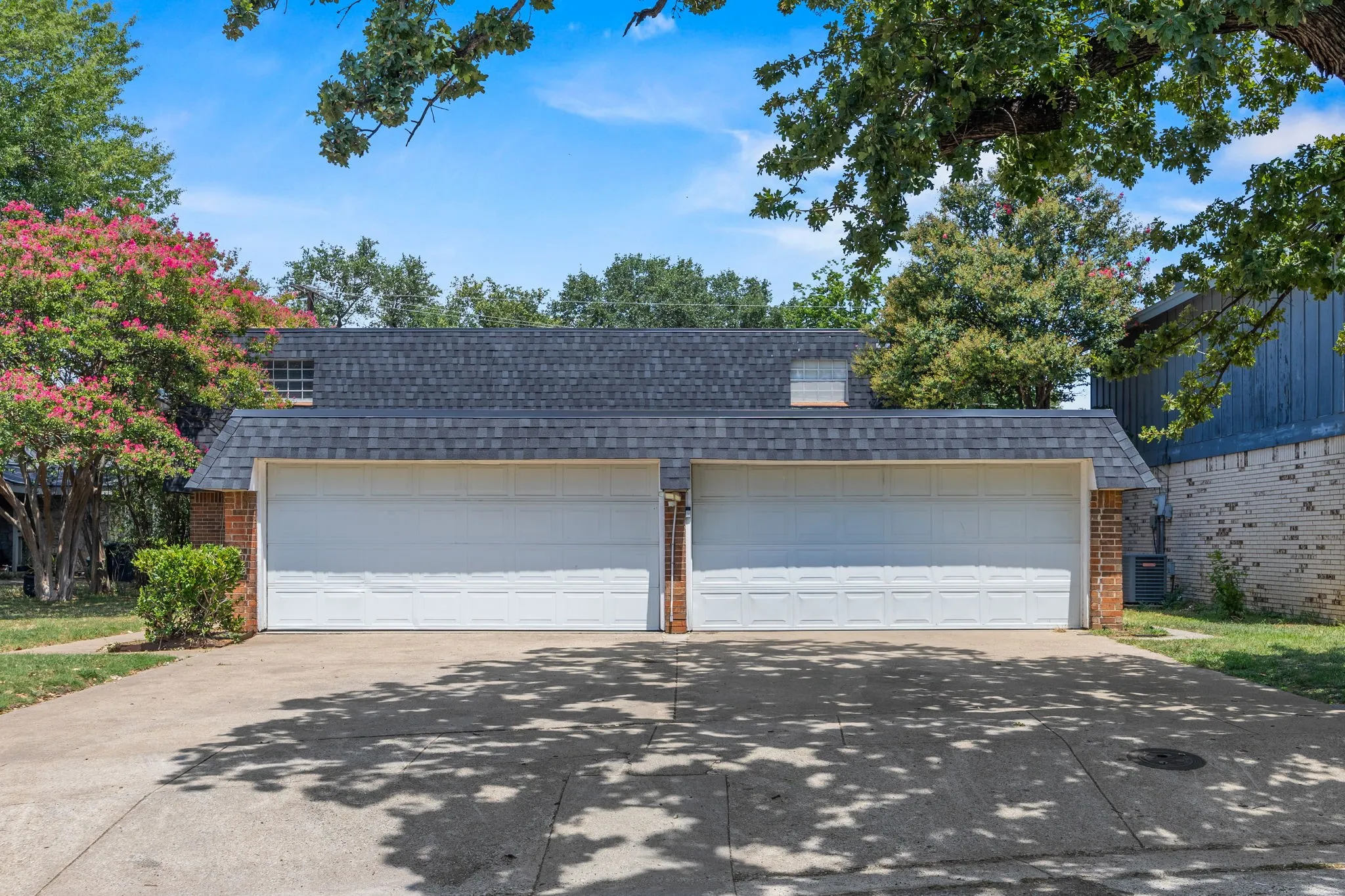 Brick exterior featuring a two-car garage with white doors, a dark shingled roof, and an asphalt driveway