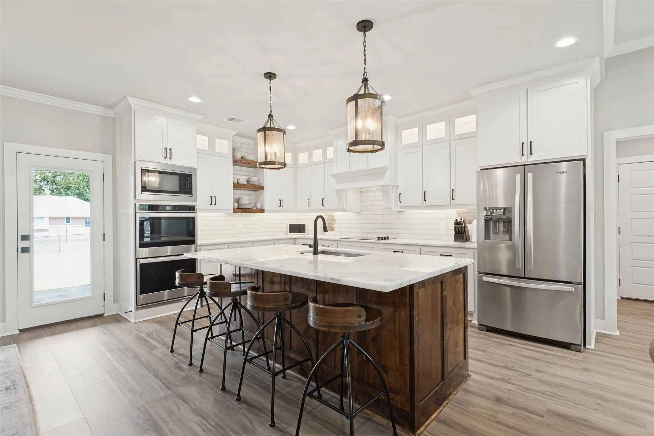 Spacious kitchen featuring a wood-finish island with a light-toned countertop, white cabinetry with dark hardware, stainless steel appliances, and wood-finish flooring
