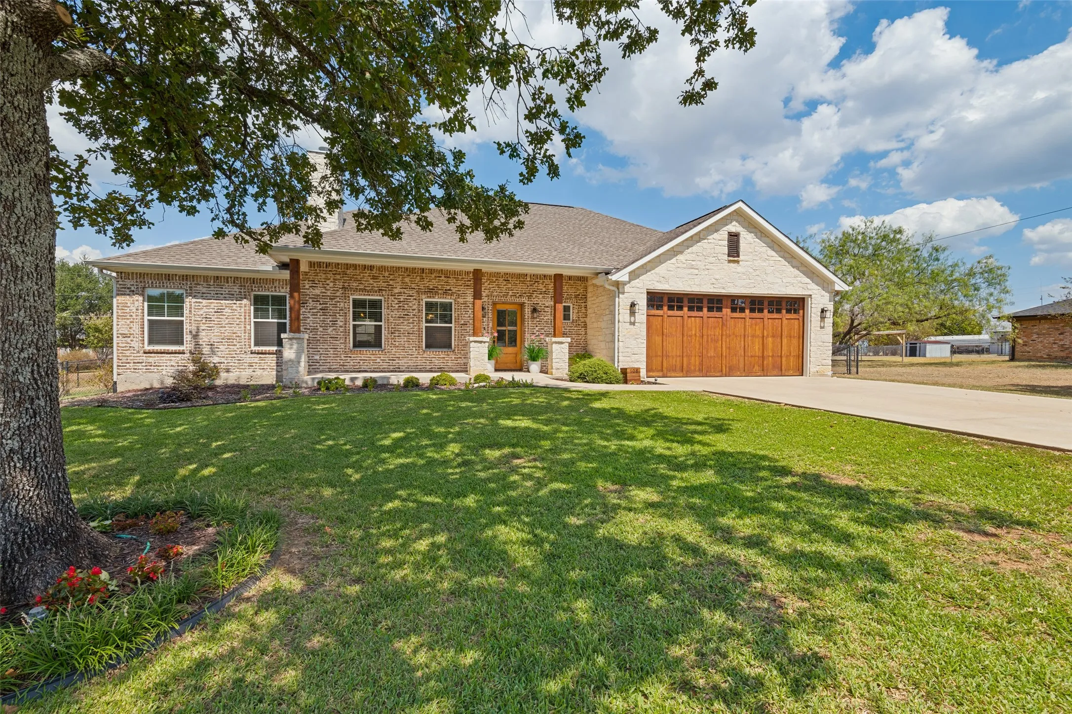 Brick exterior with stone accents, wood-finish garage door, covered front porch with wood columns, and a concrete driveway