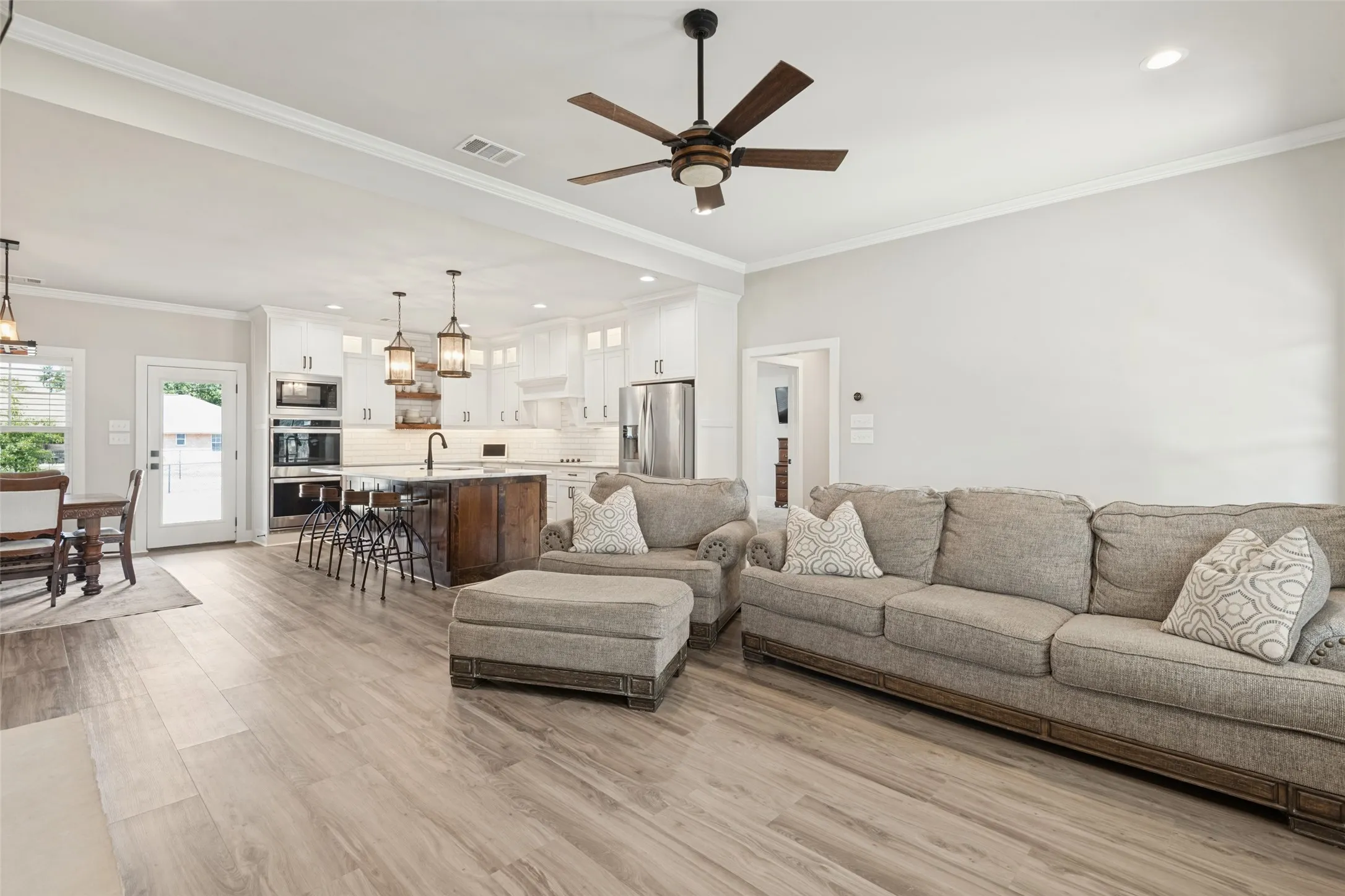 Open-concept living space featuring wood-finish flooring, crown molding, and a ceiling fan