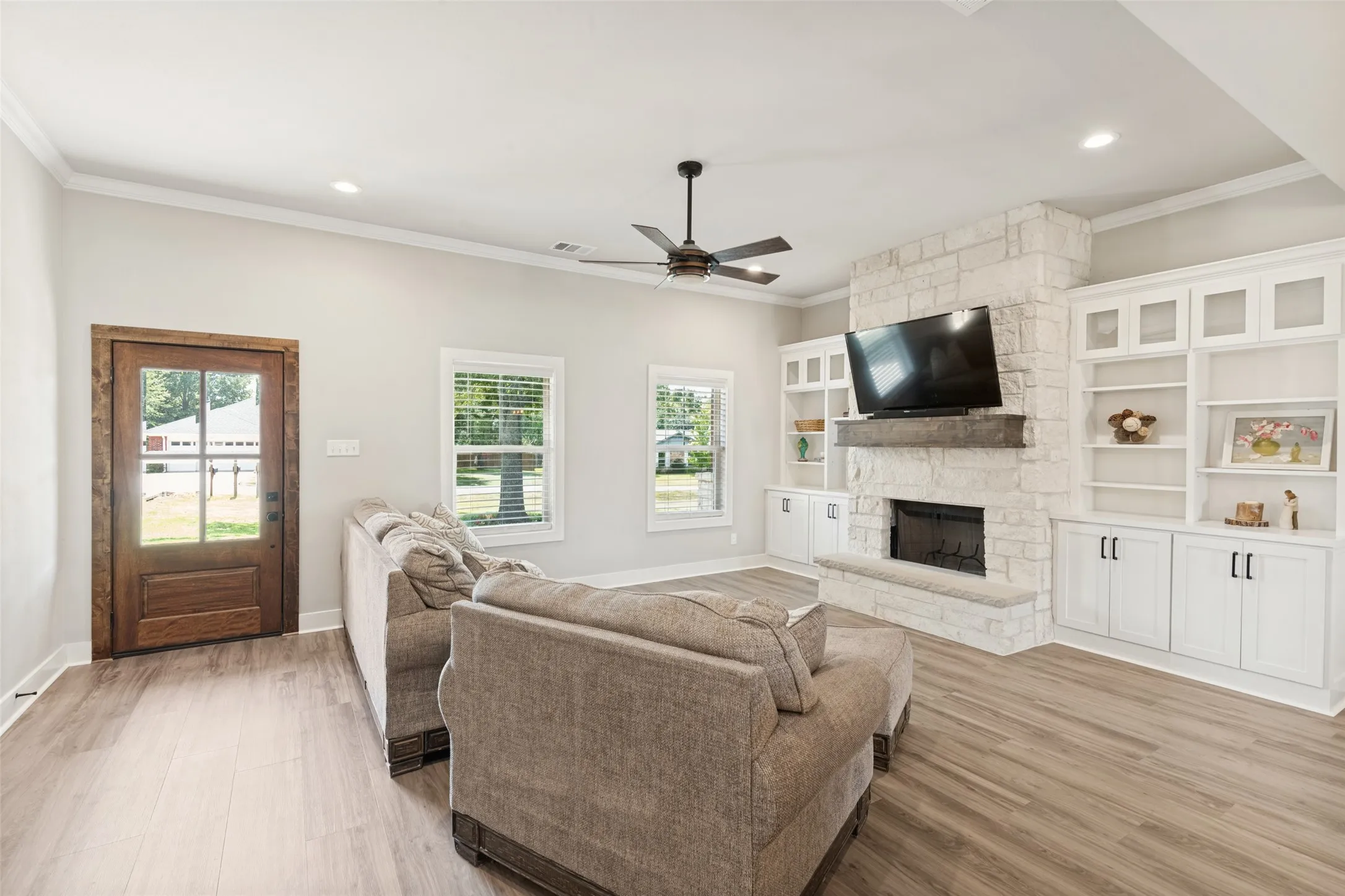 Spacious room featuring wood-finish flooring, a stone-clad fireplace, and built-in cabinetry