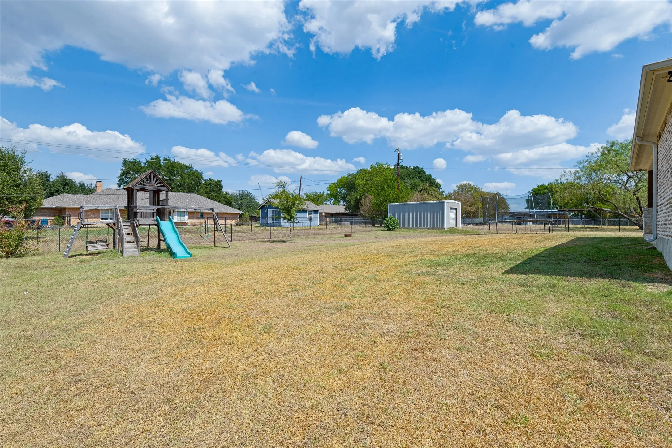 Expansive backyard featuring a fenced perimeter, a wooden playset with a slide, and a detached storage shed