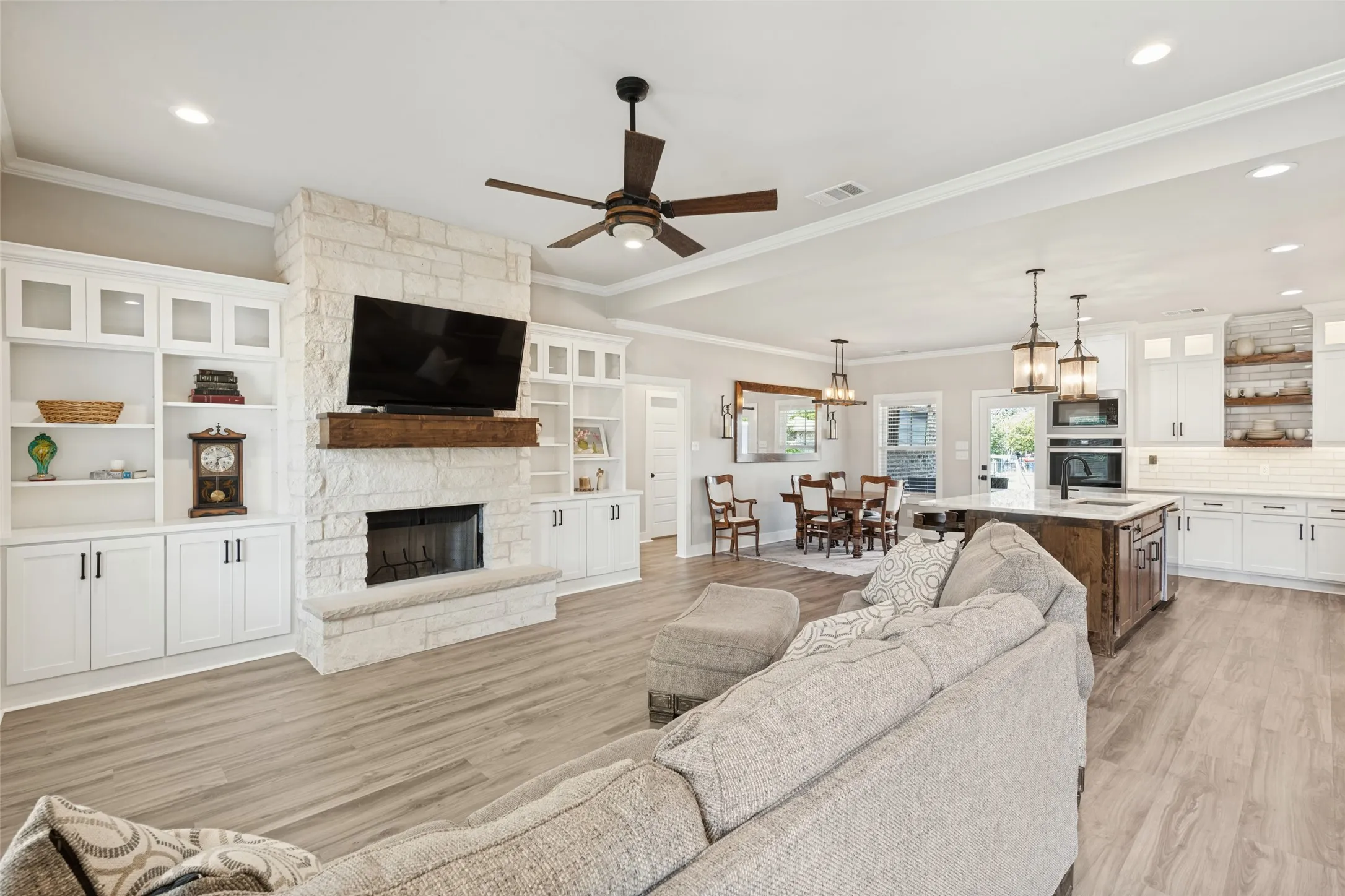 Open-concept living space featuring wood-finish flooring, a stone-faced fireplace with a wood mantle, and built-in white cabinetry