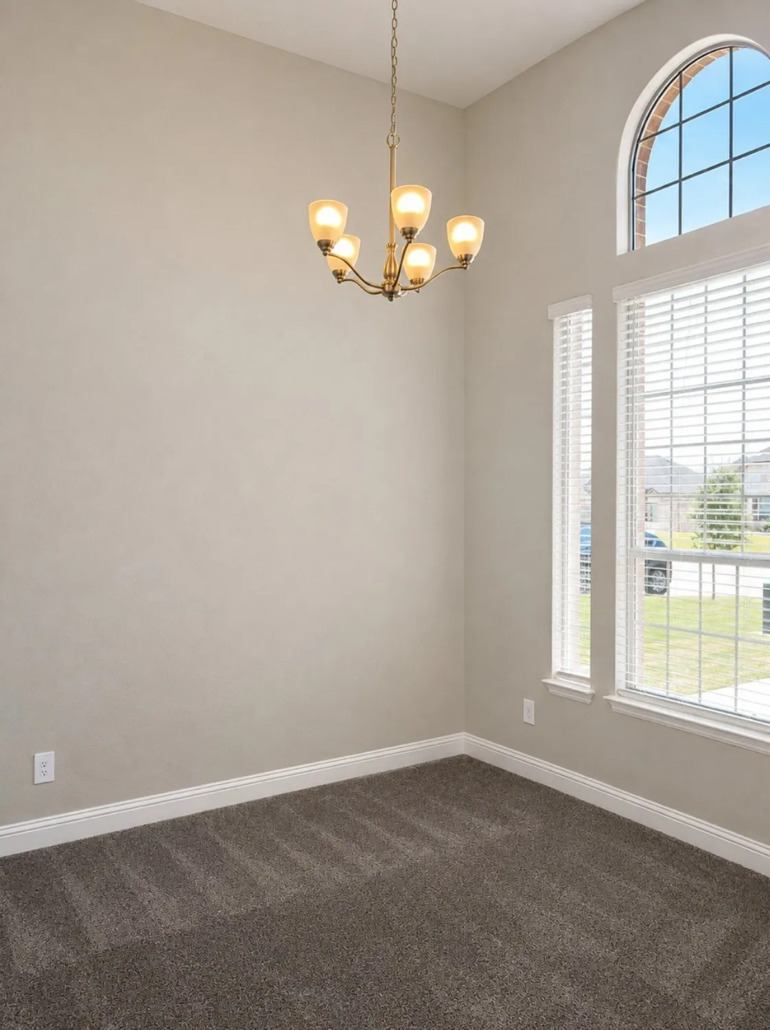 Vaulted ceiling with a five-light chandelier, arched transom window, dual pane windows, and neutral carpeting