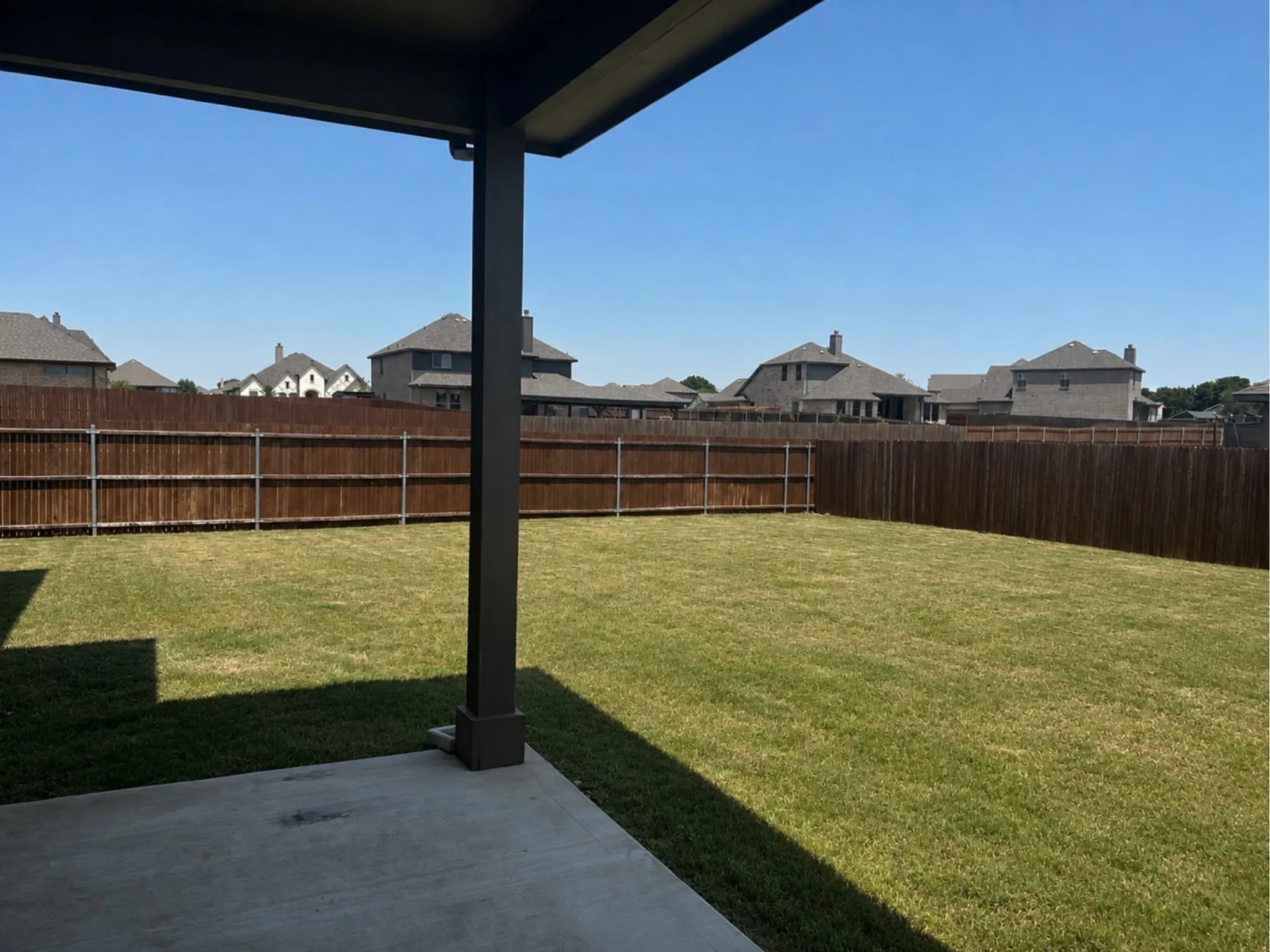 Expansive backyard featuring a manicured lawn, full privacy fencing, and a concrete patio with an overhead cover