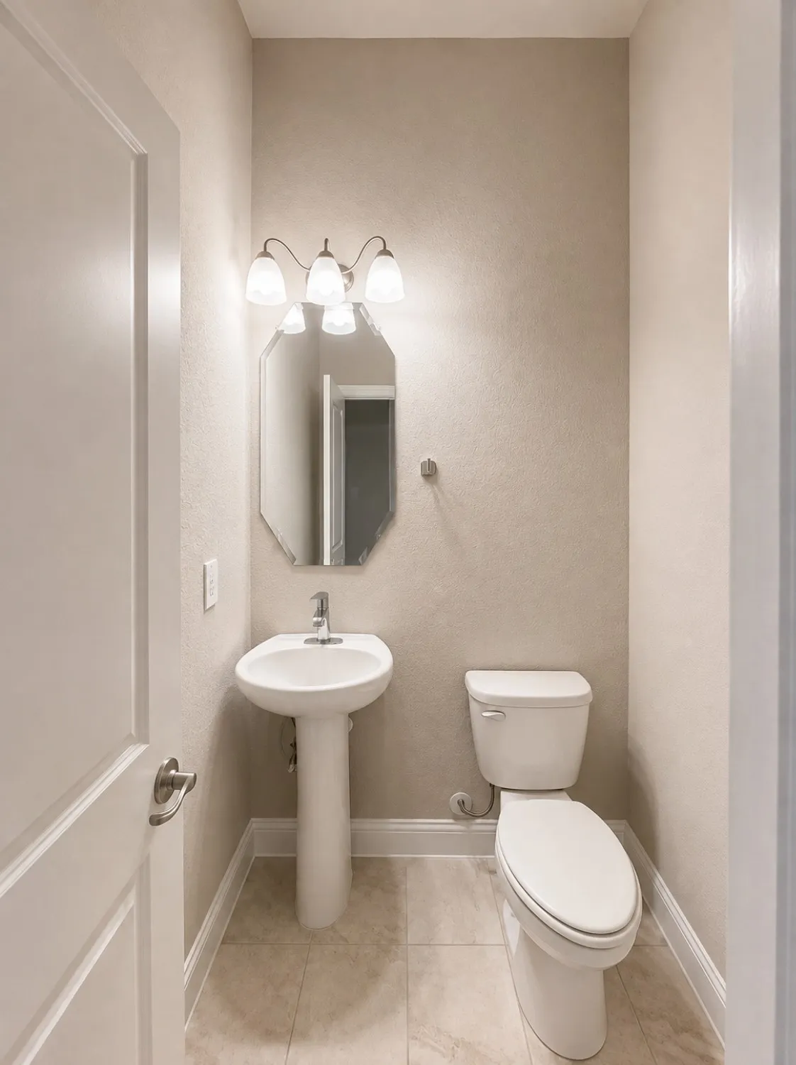 Powder room featuring a pedestal sink, a wall-mounted light fixture with three sconces, an octagonal mirror, a toilet, and light-toned floor tiling