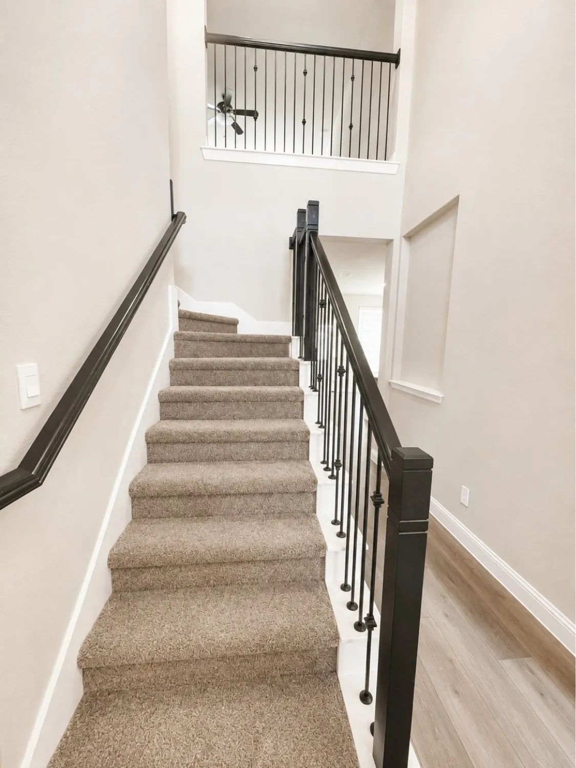 Carpeted staircase with black wrought iron balusters and dark wood newel posts