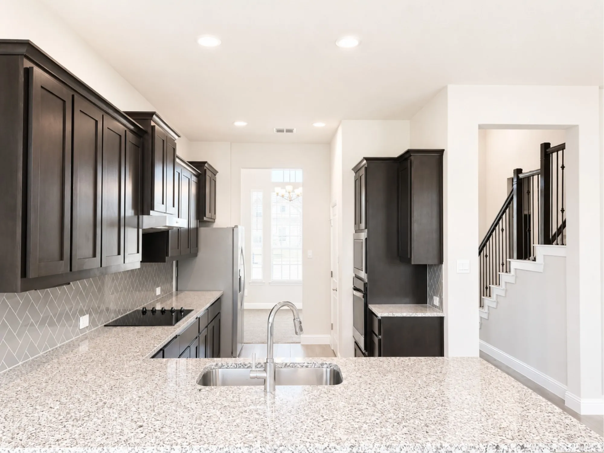 Gourmet kitchen featuring dark cabinetry with recessed panel doors, quartz countertops, a dual-basin undermount sink with polished chrome faucet, and a geometric tile backsplash