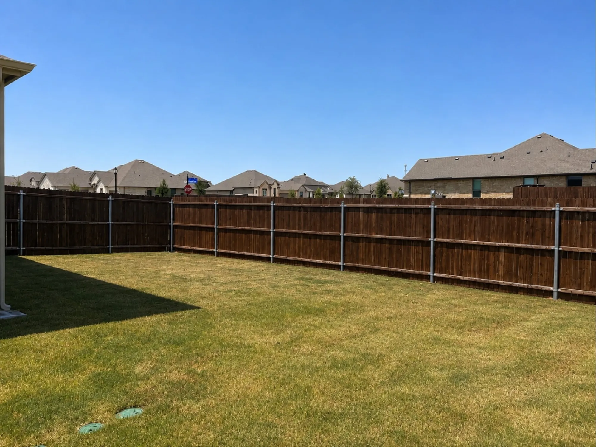 Spacious backyard featuring a level lawn with mature wood-finish fencing and metal posts, bordered by residential properties