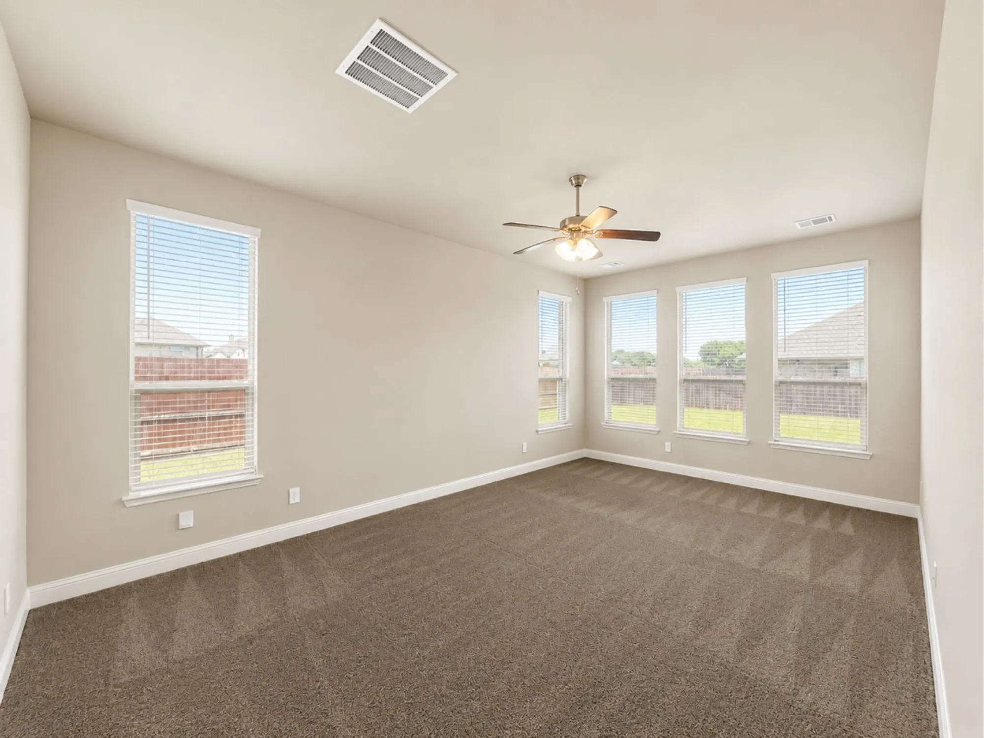 Spacious room featuring multiple windows, neutral wall tones, plush carpeting, a ceiling fan with integrated lighting, and white baseboards