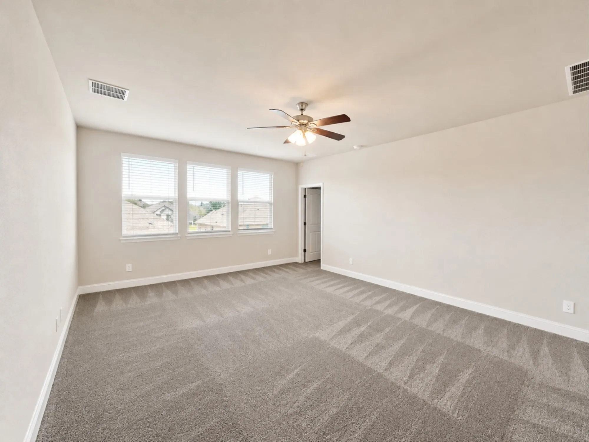 Spacious room featuring neutral paint, gray carpeting, triple windows with blinds, a ceiling fan, and white trim