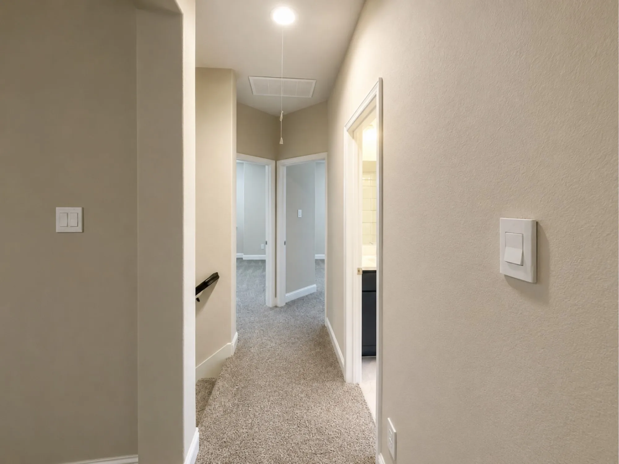 Carpeted hallway with light neutral walls, white baseboards, and multiple doorways leading to additional rooms