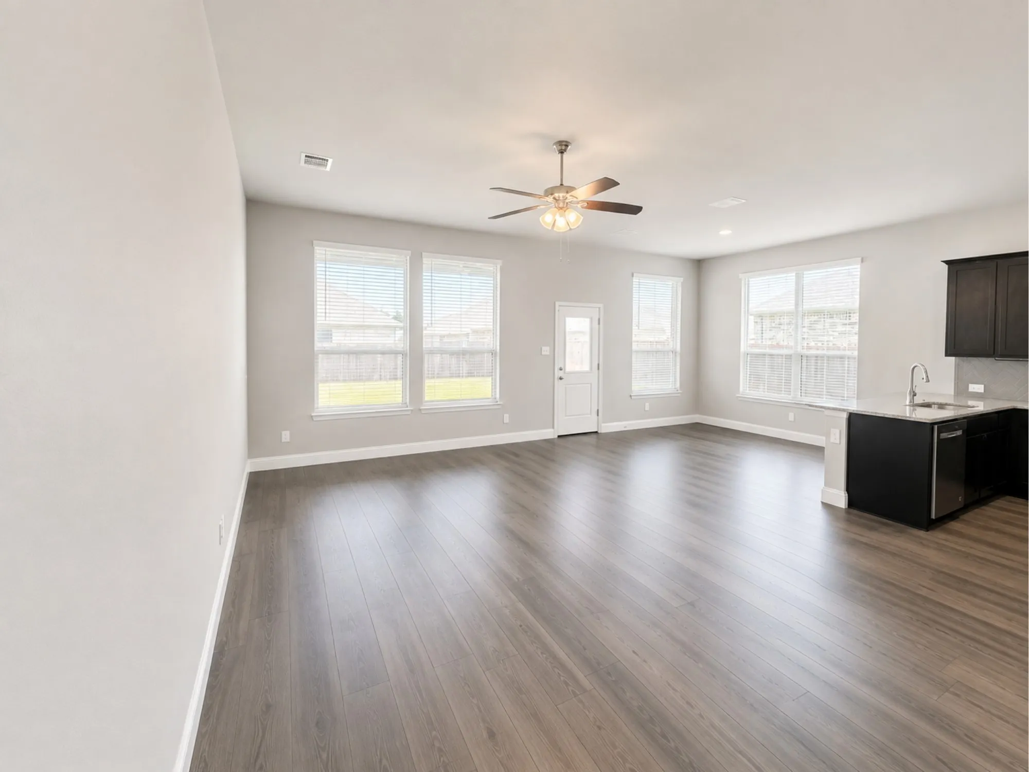 Open-concept living space featuring wood-finish flooring, multiple large windows, and a ceiling fan