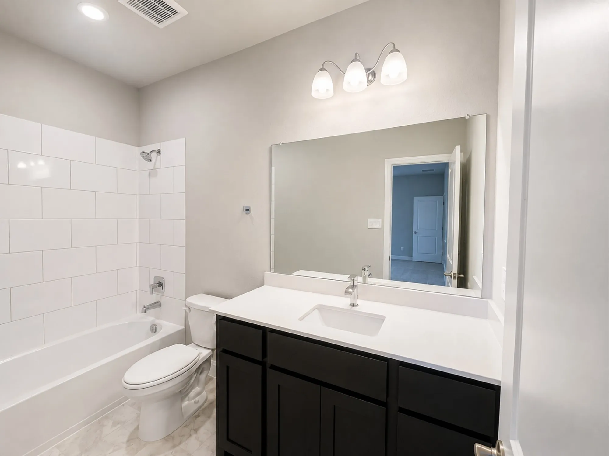 Spa-inspired primary bathroom featuring a double-sink vanity with black cabinetry, white quartz countertop, and polished chrome fixtures