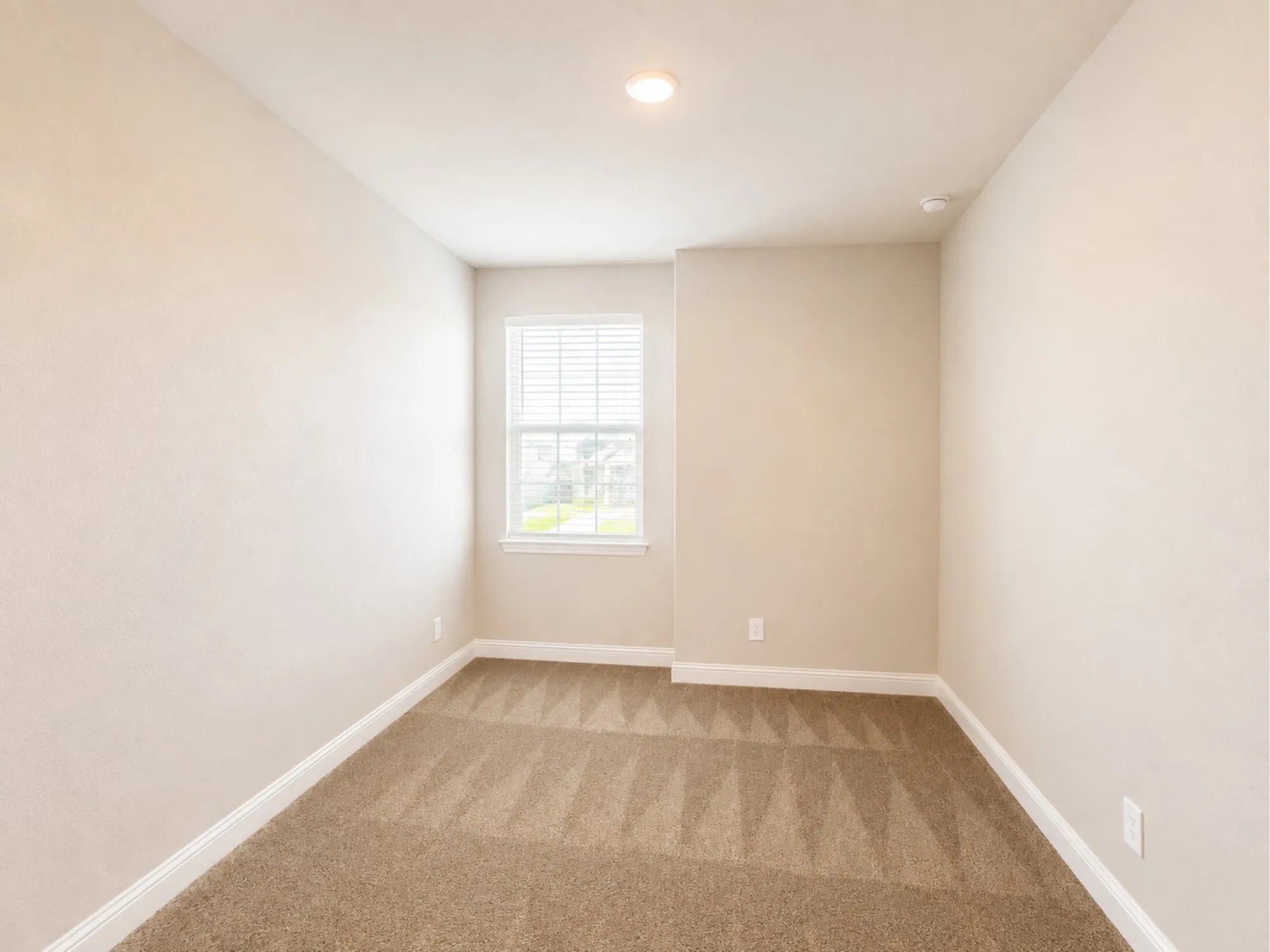 Interior room featuring a single window with blinds, neutral wall paint, and patterned carpet flooring