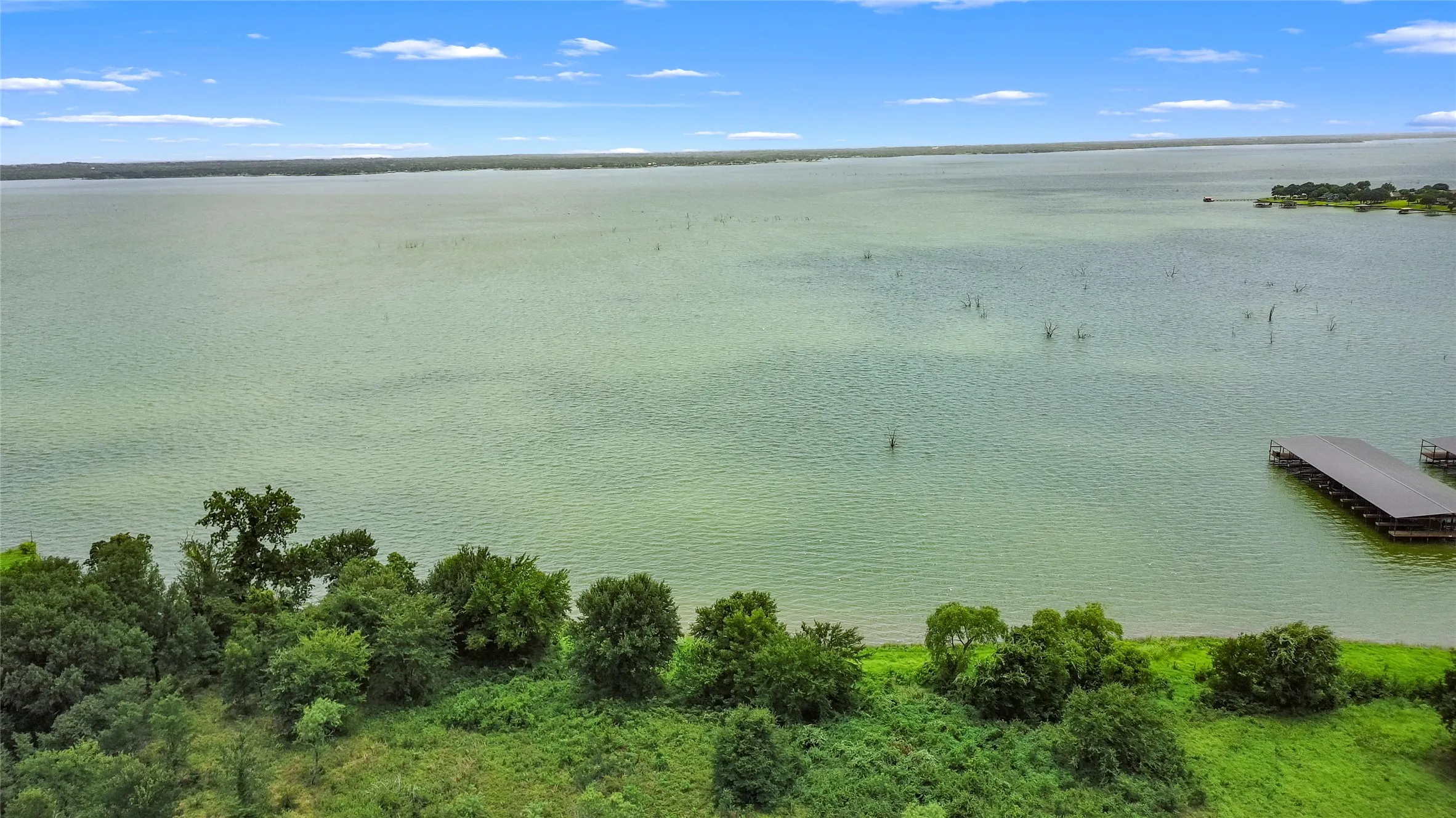 Expansive waterfront property with a private dock structure, abundant mature trees, and a clear blue sky overhead