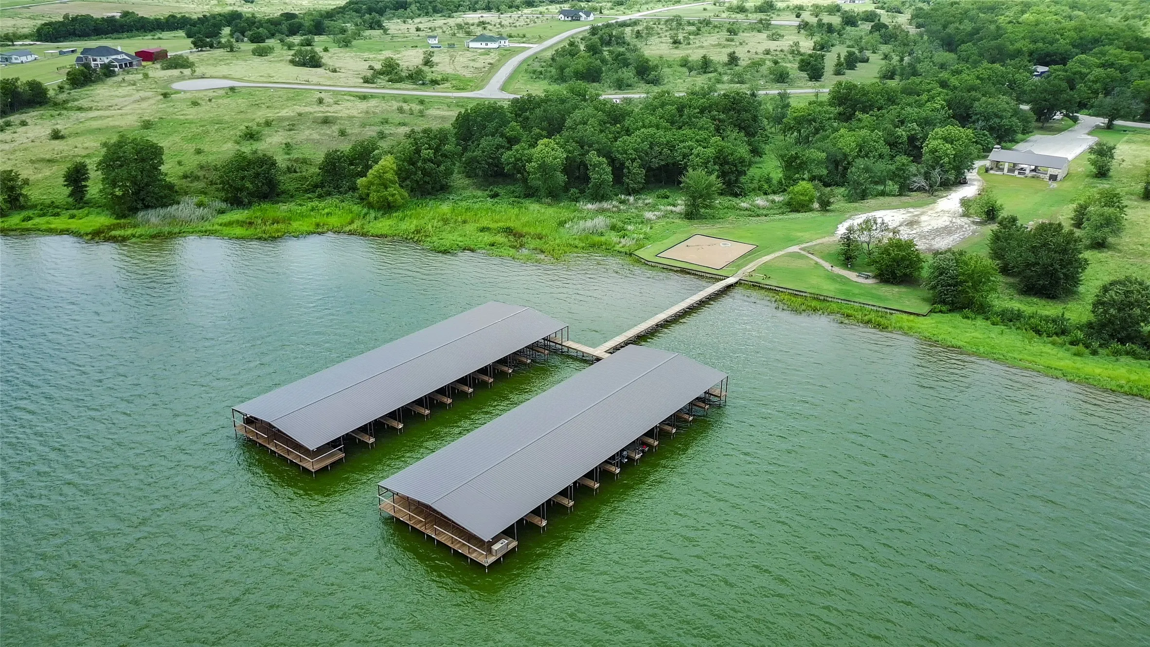 Two covered boat docks with multiple slips, a wooden pier, and a sandy recreational area