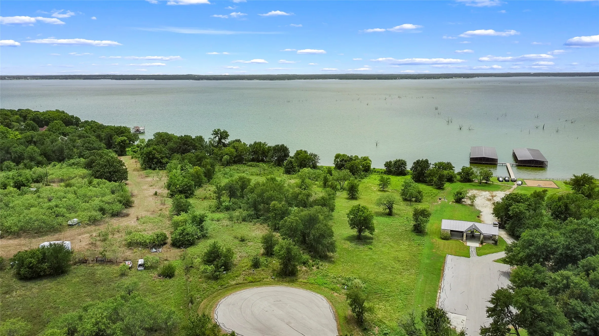 Lakefront property featuring expansive green spaces, mature trees, a dedicated boat dock with covered slips, and a paved access road