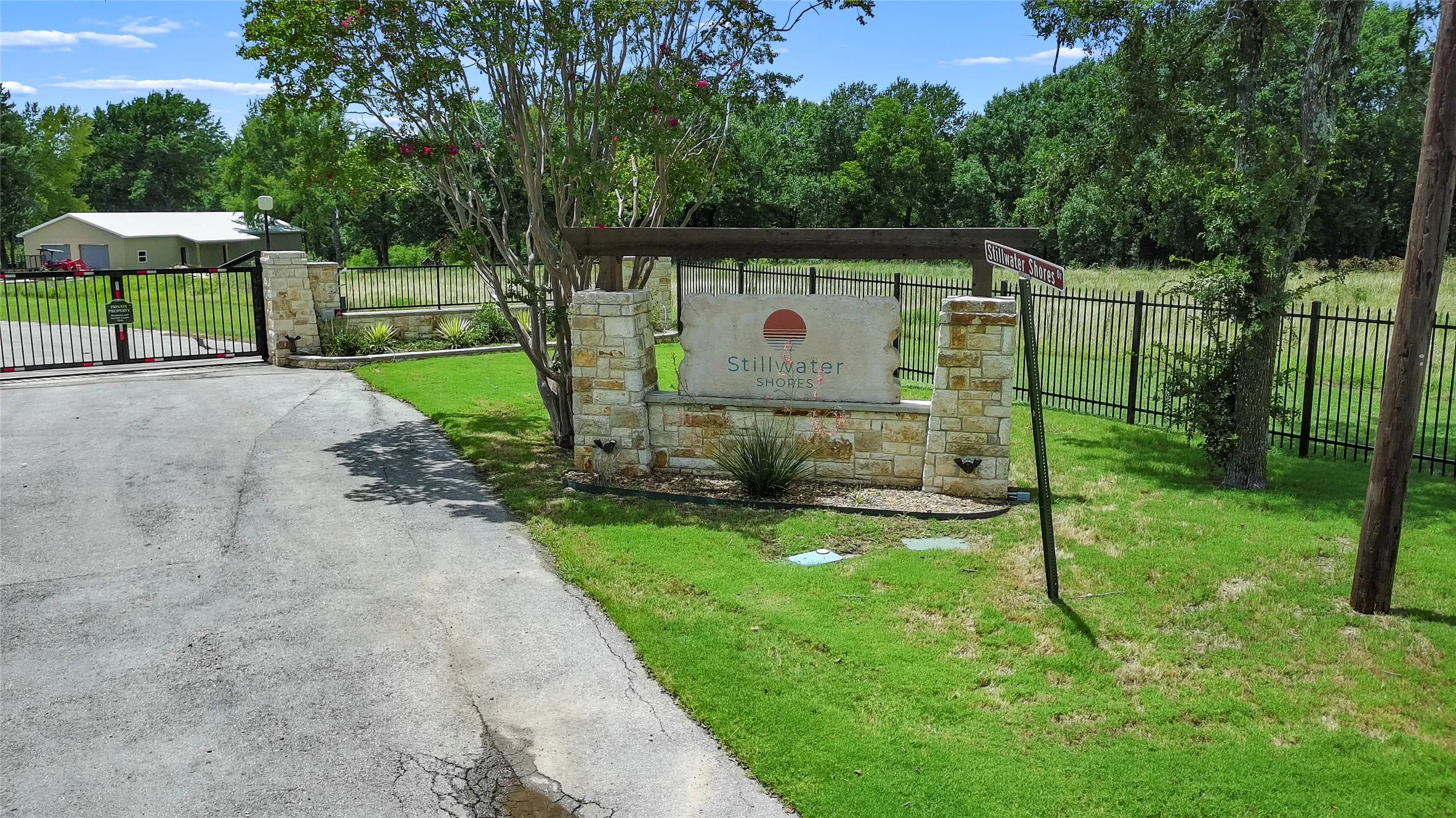 Entry features a stone and wood-beam monument sign, a wrought iron gate with stone pilasters, and a black metal perimeter fence