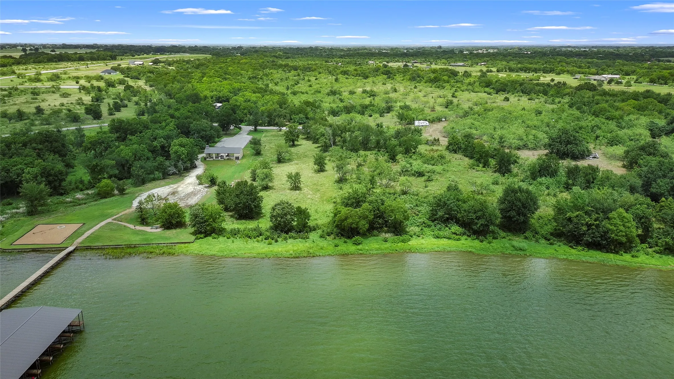 Property featuring a waterfront location, a private dock with covered boat slips, a sandy beach area, and expansive green spaces with mature trees