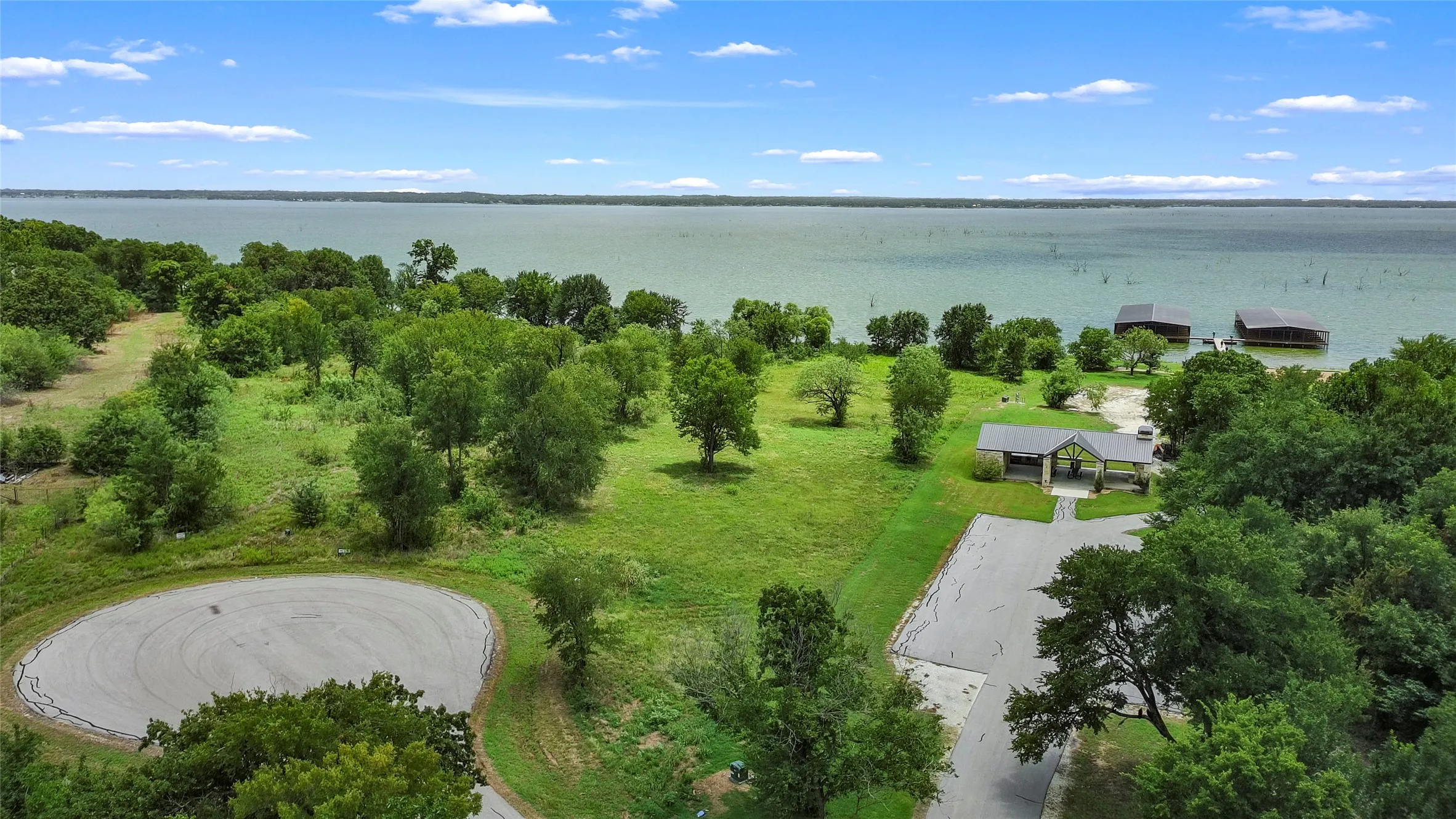 Lakefront property featuring a large body of water, extensive green spaces, mature trees, and a paved road