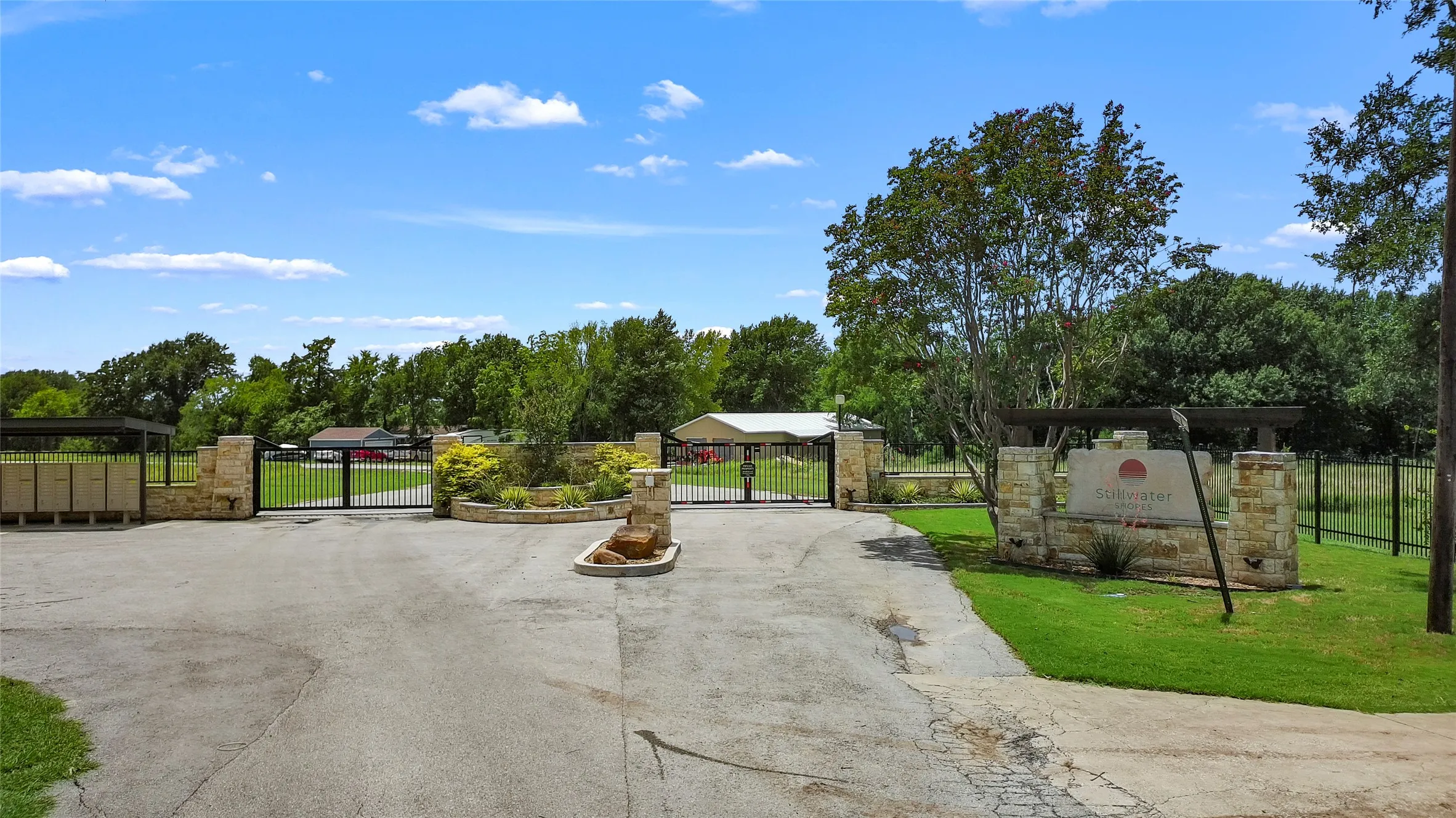 Stone-clad entry columns with dual wrought iron gates and a paved access road