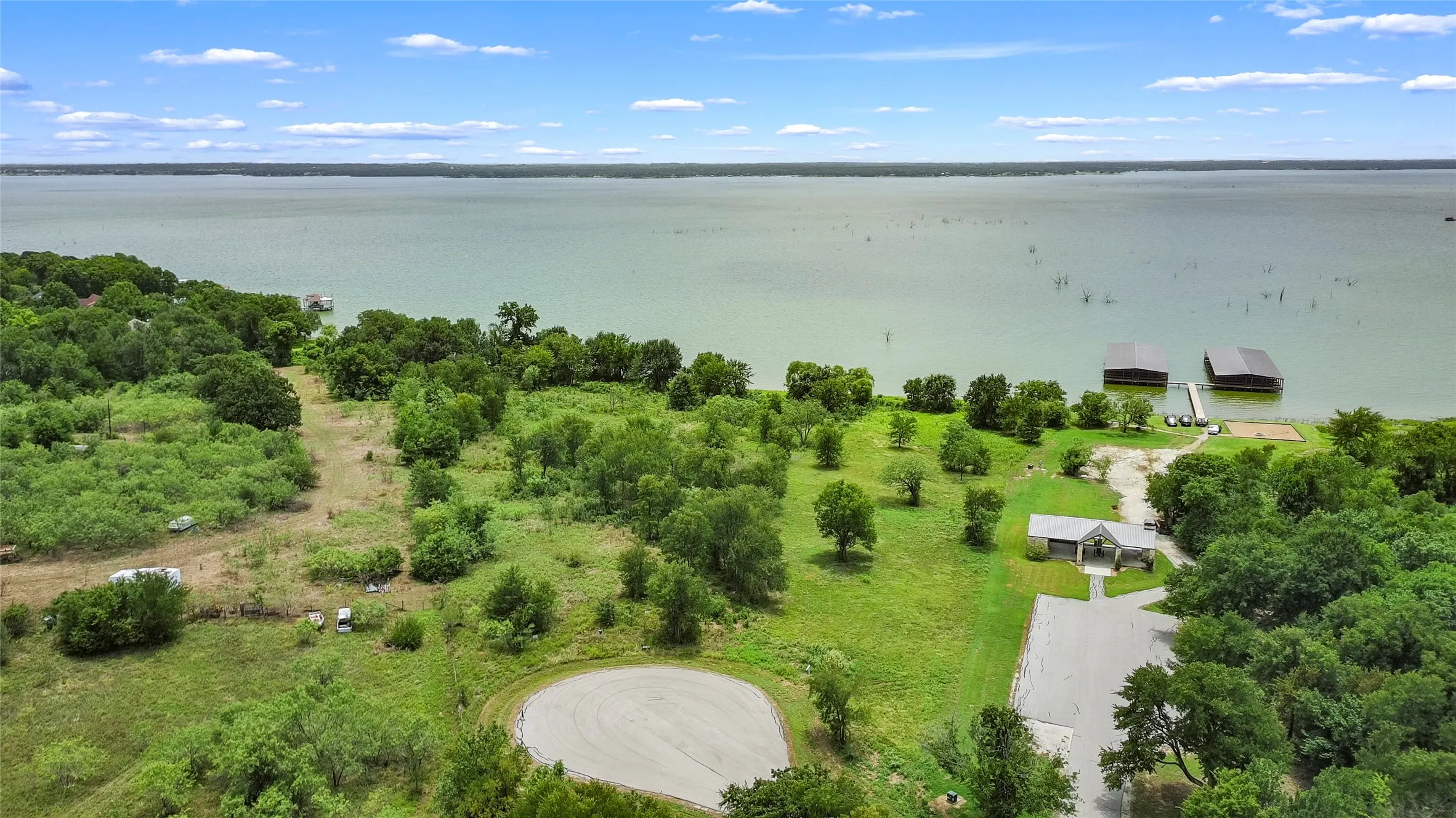 Expansive waterfront property featuring a large lake, multiple boat docks, a paved parking area, and a structure with a covered entrance