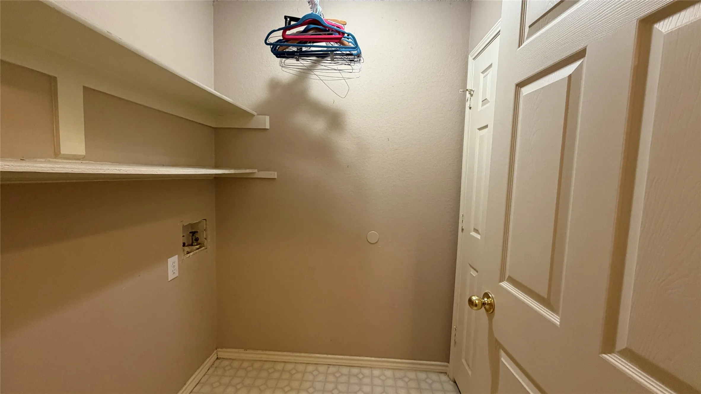 Laundry area with built-in shelving, patterned floor tiles, and a panel door with a brass-finish knob