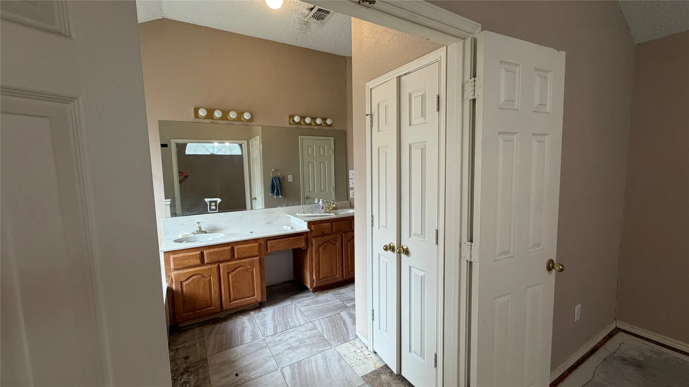 Vaulted ceiling, dual vanity, wood-finish cabinetry, built-in makeup vanity, and tile flooring