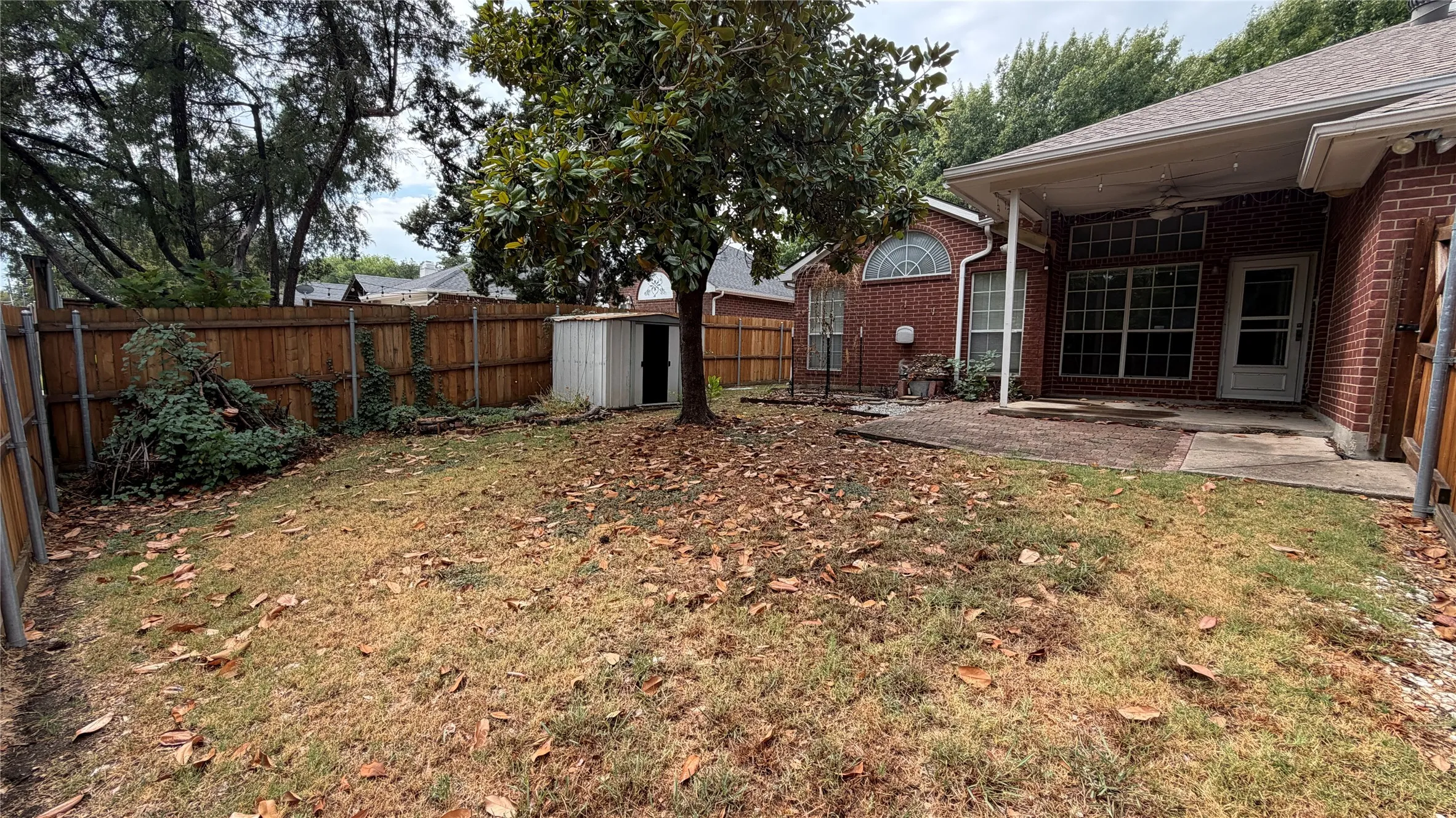 Expansive backyard featuring a wood privacy fence, mature trees, and a covered patio