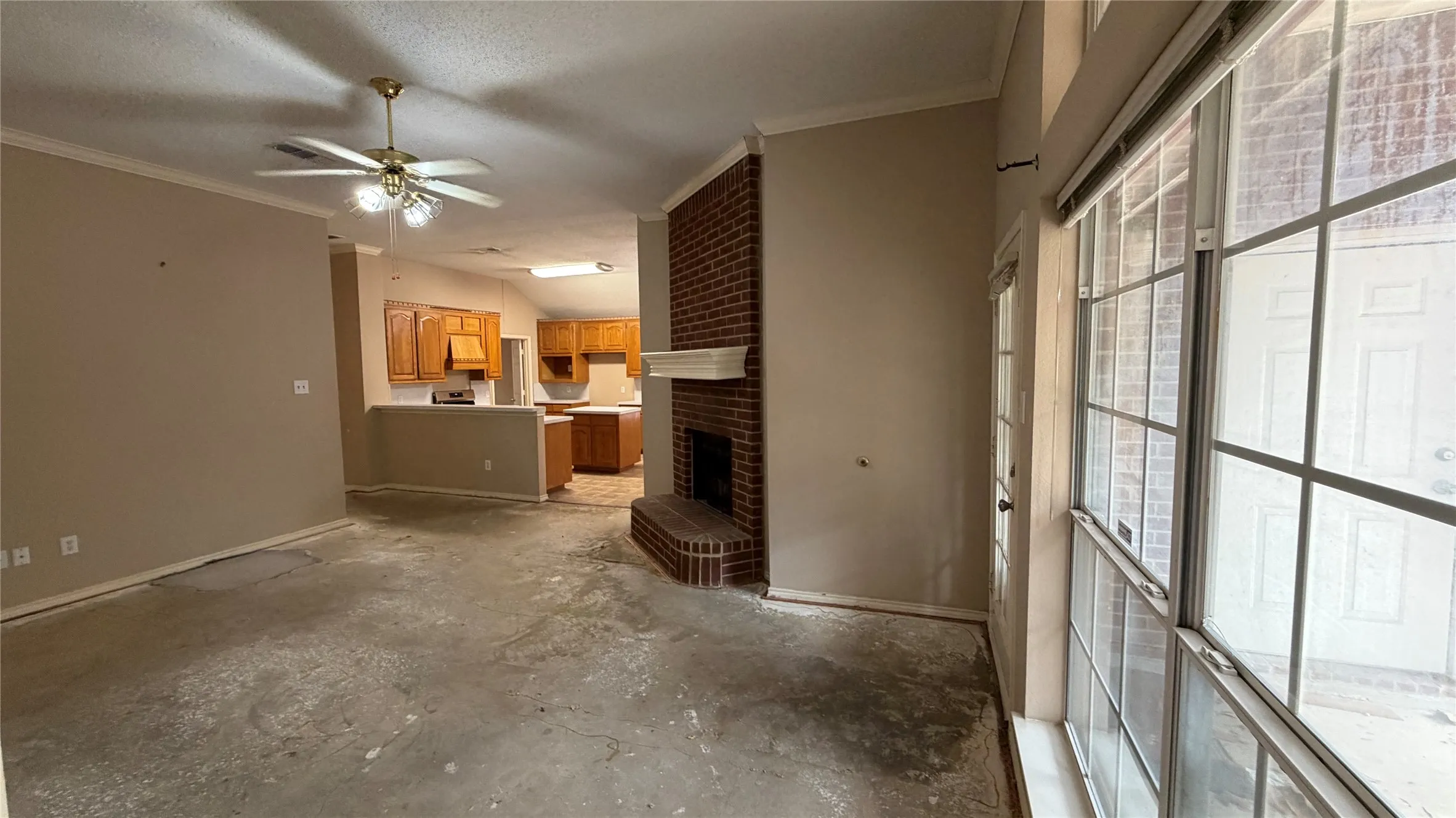 Living area with exposed subfloor, brick fireplace with mantel, and ceiling fan
