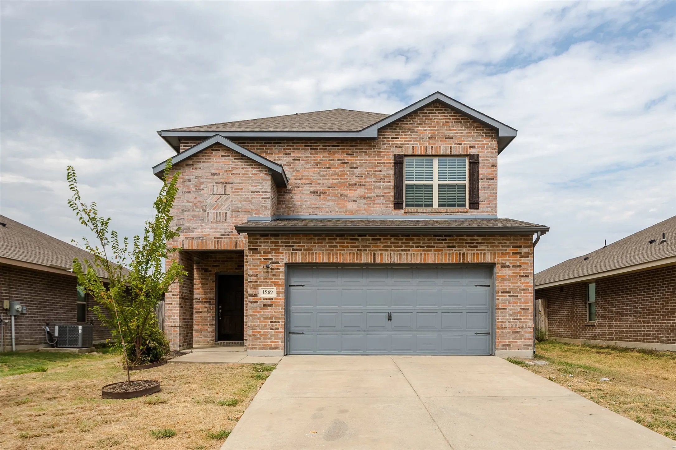 Brick facade with a two-car garage, concrete driveway, and covered entry