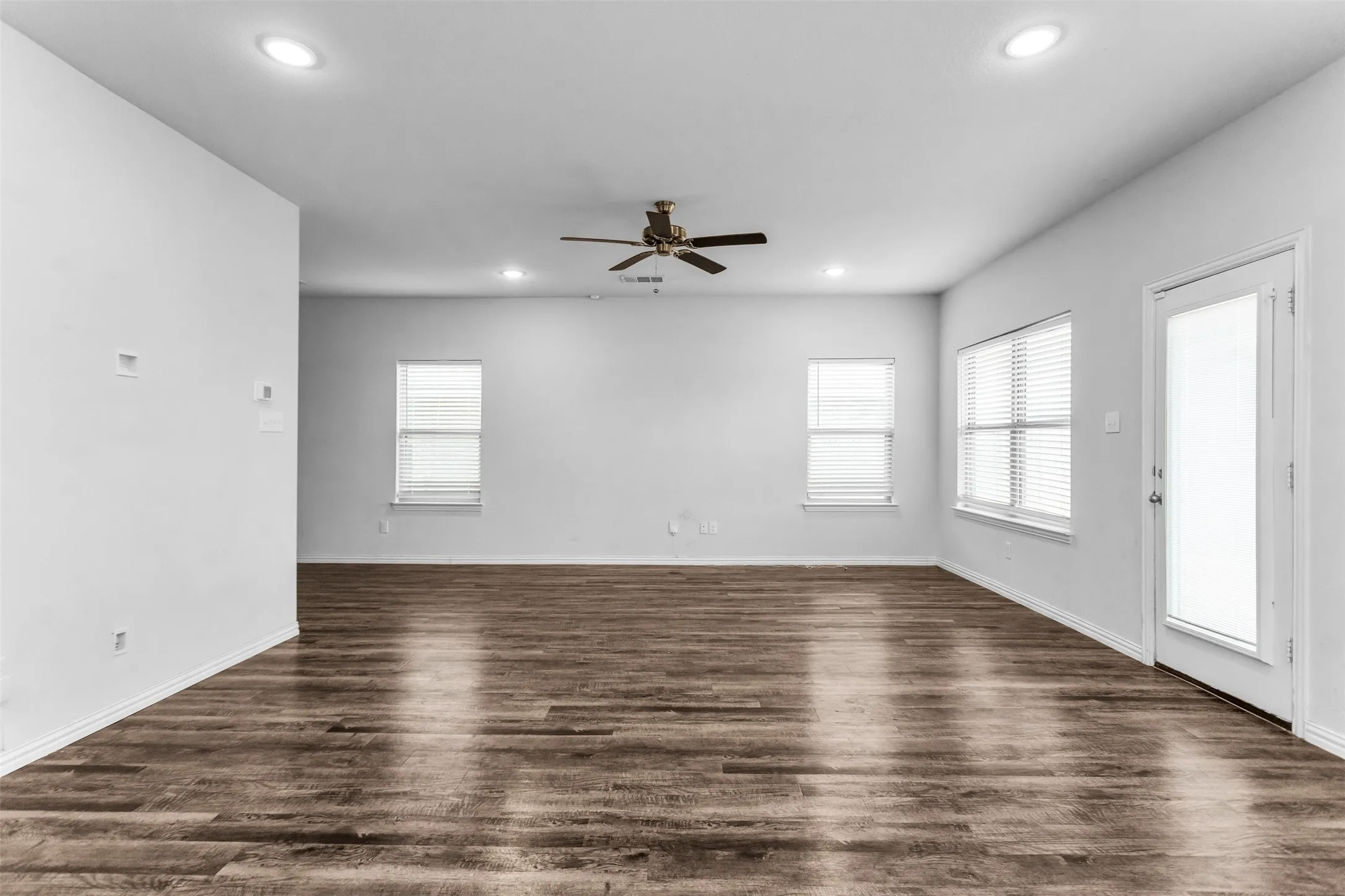 Wood-finish flooring, recessed lighting, ceiling fan, multiple windows, and a glass-paneled door