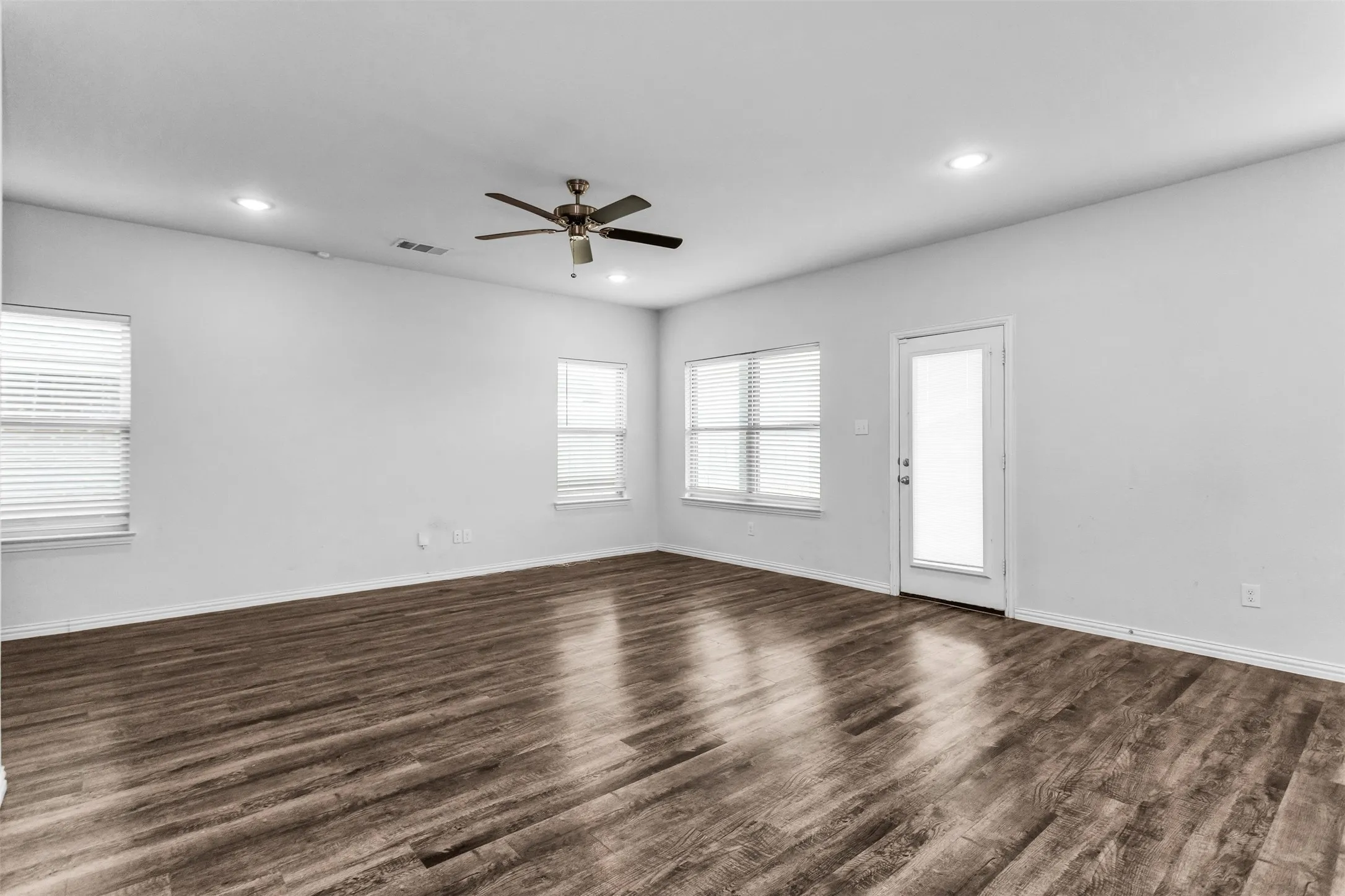 Spacious room featuring wood-finish flooring, multiple windows with blinds, a ceiling fan, and recessed lighting